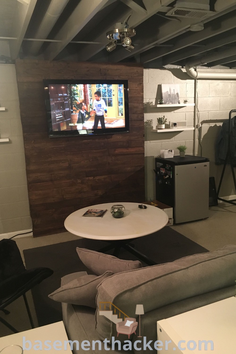 A cozy basement living room with furniture, a flat-screen TV mounted on cement walls, showcasing stylish bonus room design ideas for families. Perfect for ultimate entertaining, this area represents innovative ideas for designing a functional home and offers decor insights at basementhacker.com.