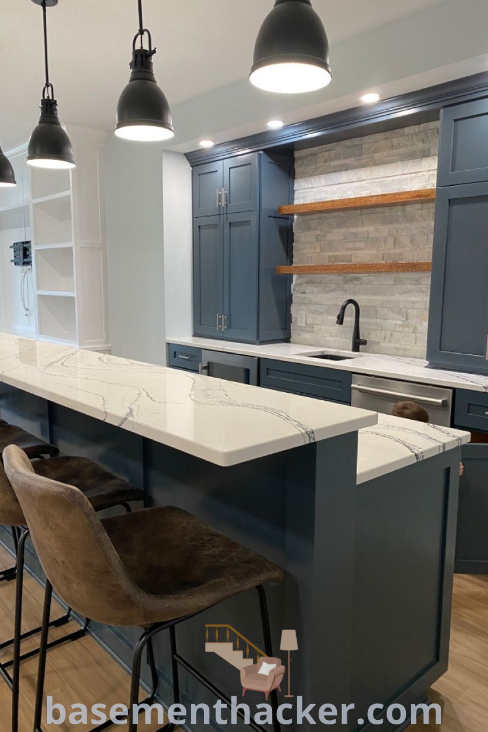 A beautifully designed navy blue basement bar featuring Cambria quartz countertops, a Silgranit sink, and custom cabinets in “Lead Gray” by Benjamin Moore. Ideal for ultimate entertaining, this space showcases modern basement makeover ideas and stylish bonus room design ideas for families. Explore more at basementhacker.com.