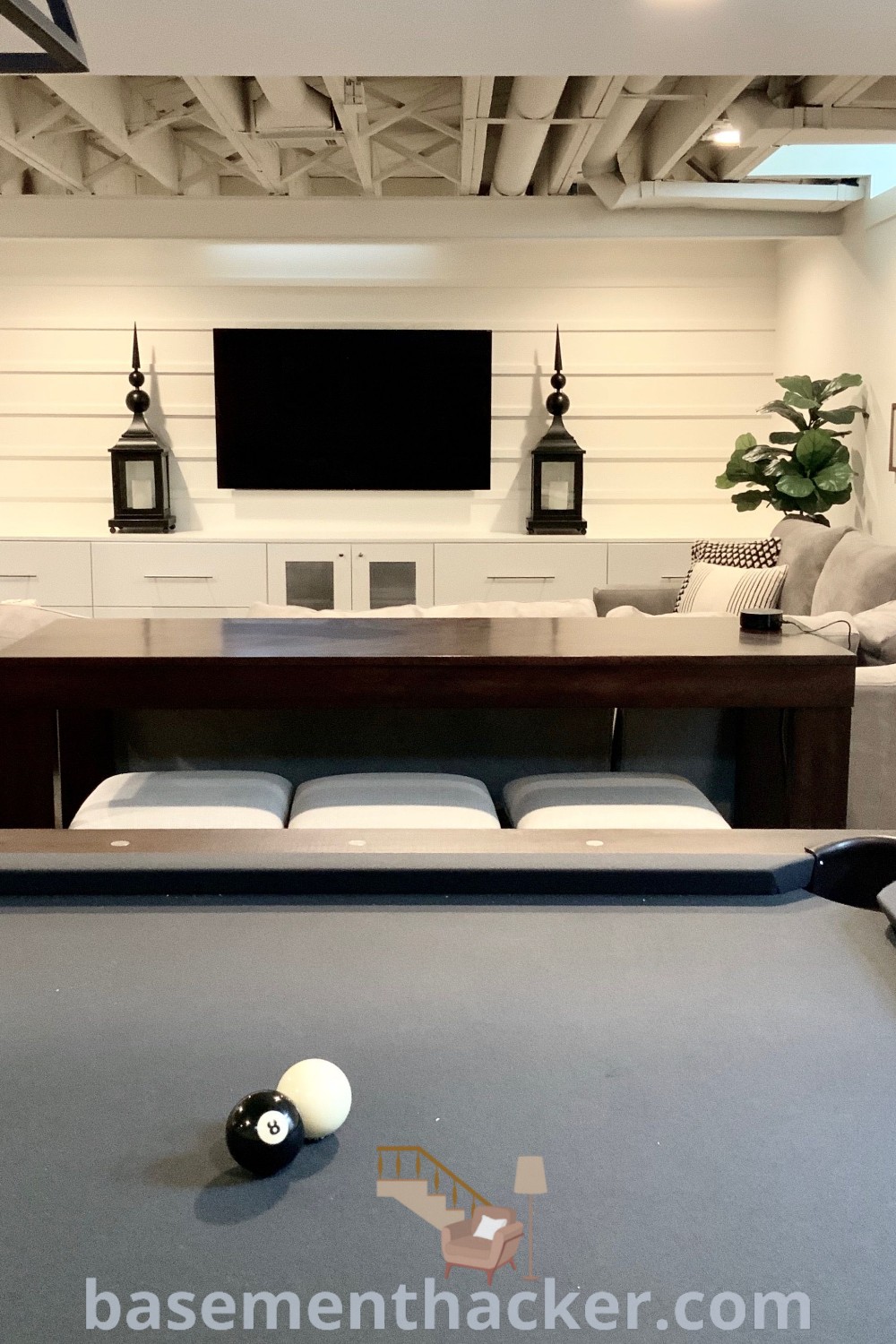 A pool table in a cozy living room surrounded by couches and a flat-screen TV, showcasing stylish bonus room design ideas for families. This image offers innovative ideas for basement refresh that are perfect for ultimate entertaining, featuring decor inspirations from basementhacker.com.