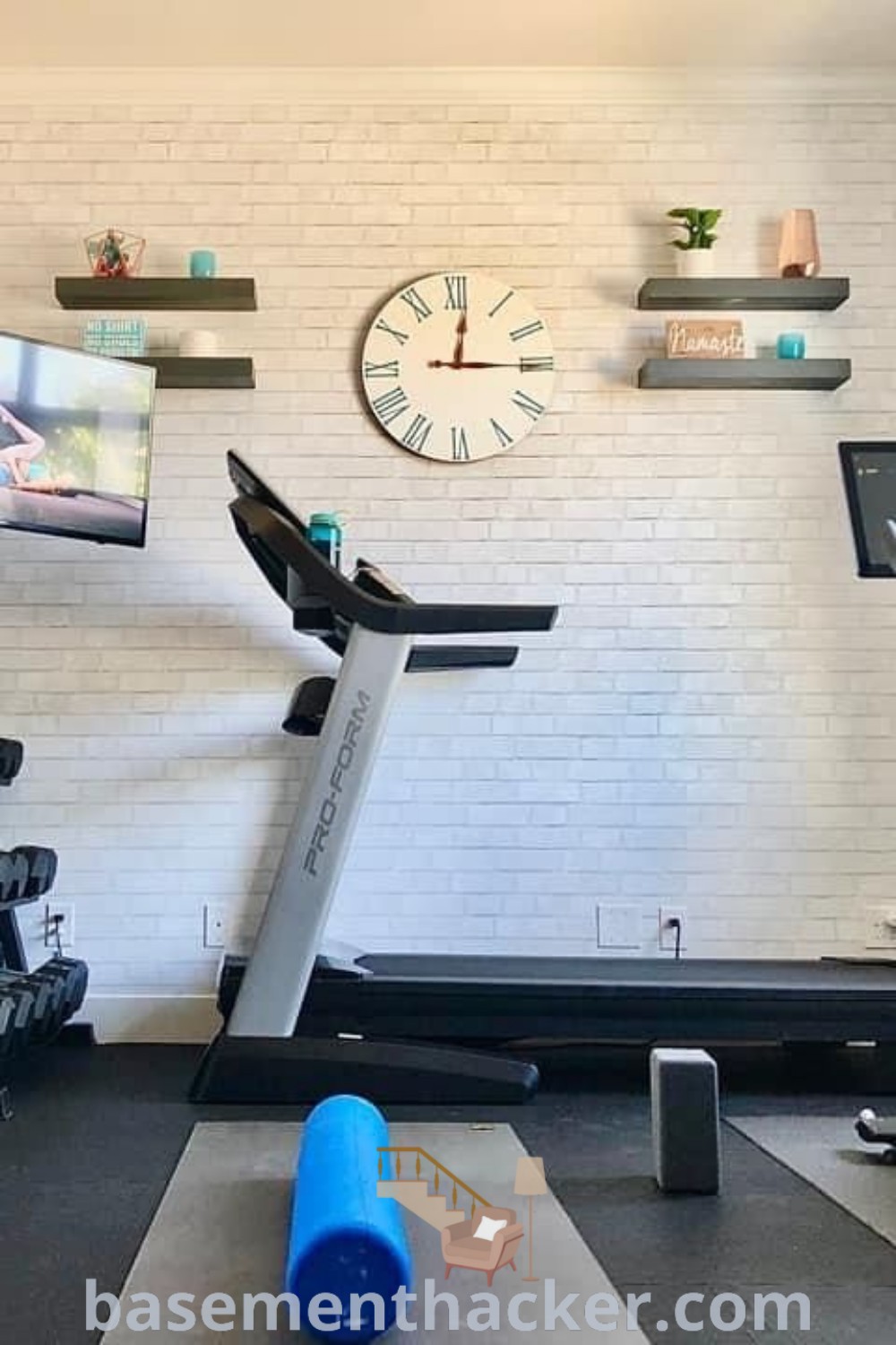 A small home gym with a treadmill, exercise bikes, and a flat screen TV, showcasing innovative ideas for designing a stylish and functional workout space. This aesthetic home gym room is perfect for small bedroom home gym inspirations. For more ideas, visit basementhacker.com.