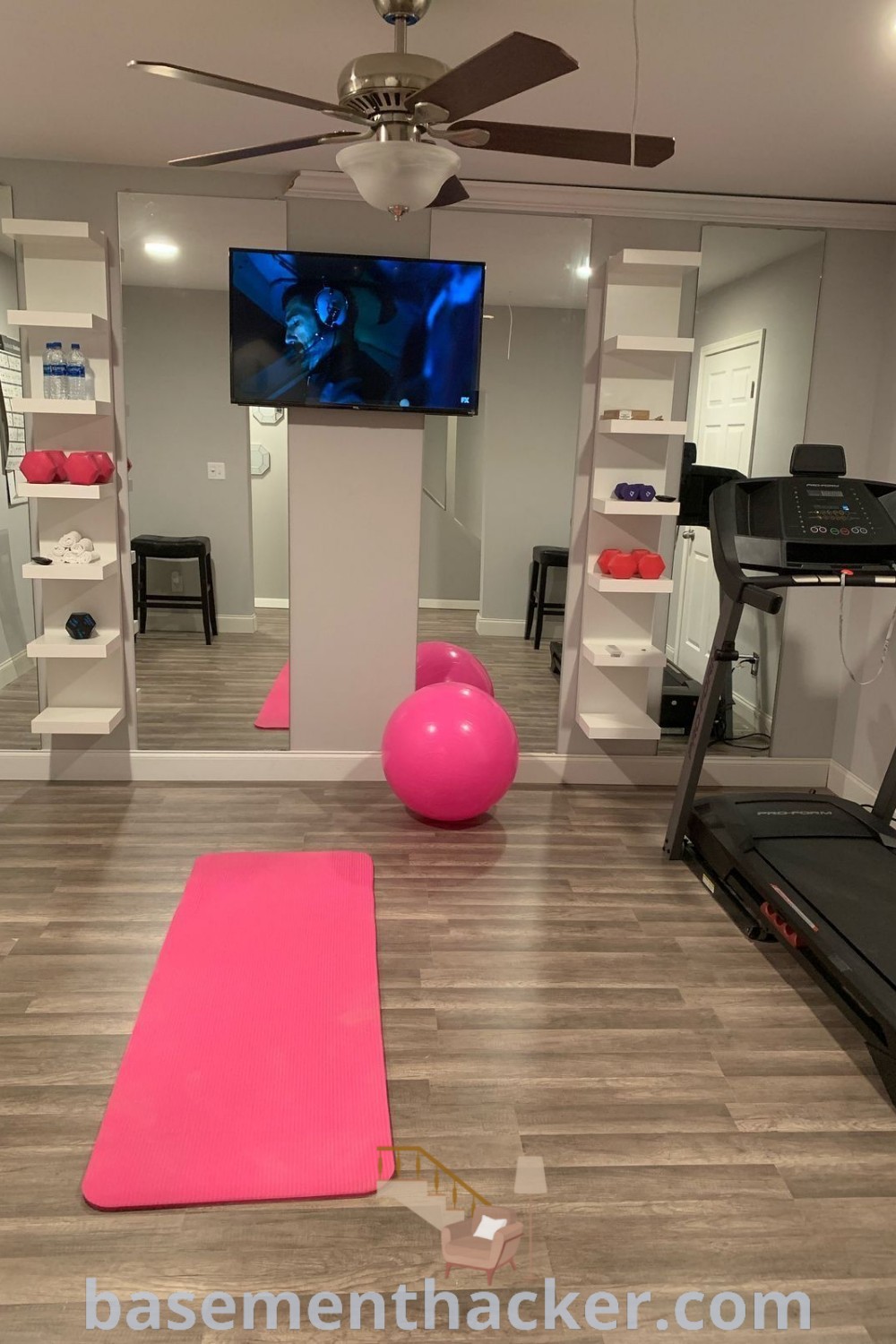 A cozy home gym setup with exercise equipment, a pink yoga mat, and a television, showcasing innovative ideas for designing a workout space. This inspiring atmosphere is ideal for cute at-home gym ideas and goals that promote health and wellness, as featured on basementhacker.com.