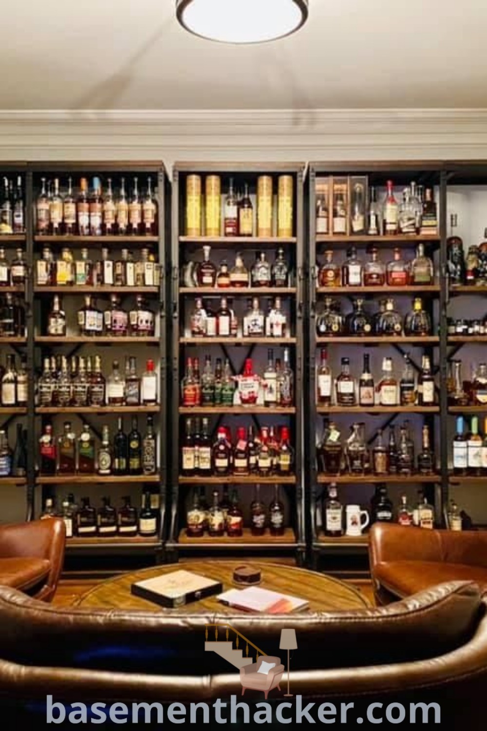 A living room showcasing a bourbon collection display on shelves filled with bottles, perfect for a cozy bourbon lounge. This stylish whiskey wall offers innovative ideas for basement makeovers and ultimate entertaining, featuring a wine bar atmosphere. Discover more creative strategies for your home at basementhacker.com.