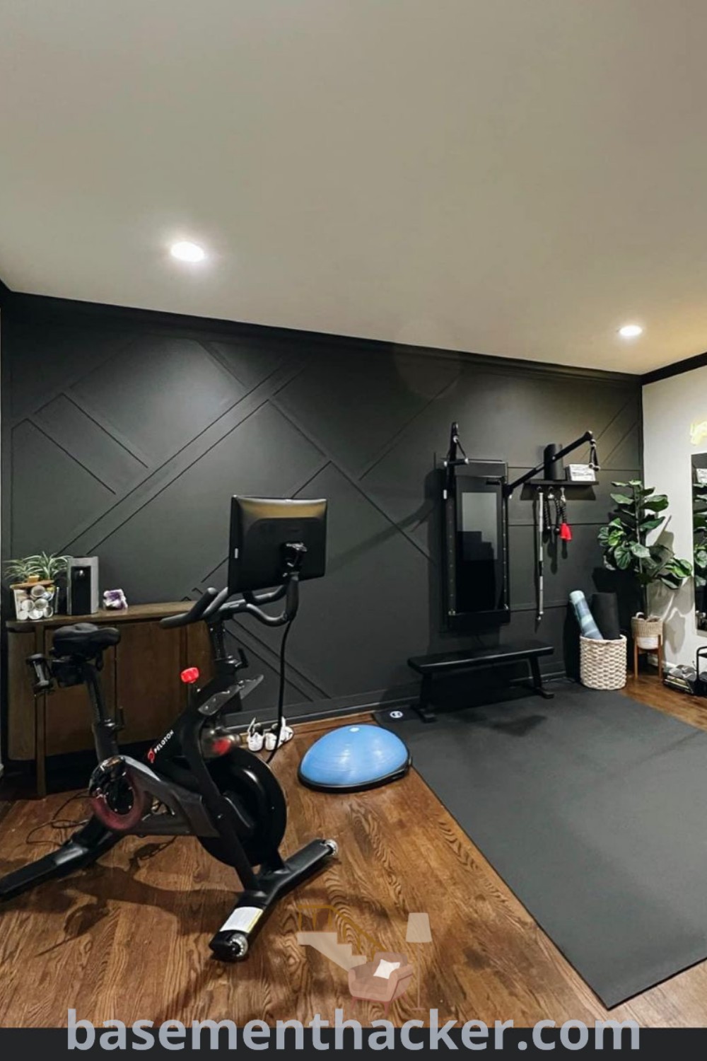 A home gym with an exercise bike, treadmill, and exercise ball on the floor, featuring stylish dark walls and vibrant accent colors. This atmospheric space showcases innovative ideas for a home gym, perfect for achieving an inspiring workout environment. Explore more at basementhacker.com for ideas to upgrade your space!