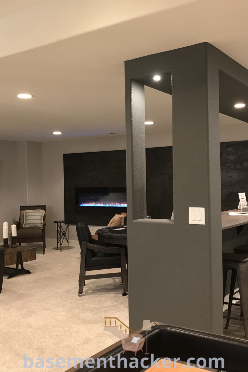 A living room in a basement filled with contemporary furniture and a flat-screen TV mounted to the wall, showcasing innovative basement makeover ideas for a stunning revamp. Perfect for stylish decor, basement pole ideas, and creating a cozy and organized home design. Explore more on basementhacker.com.