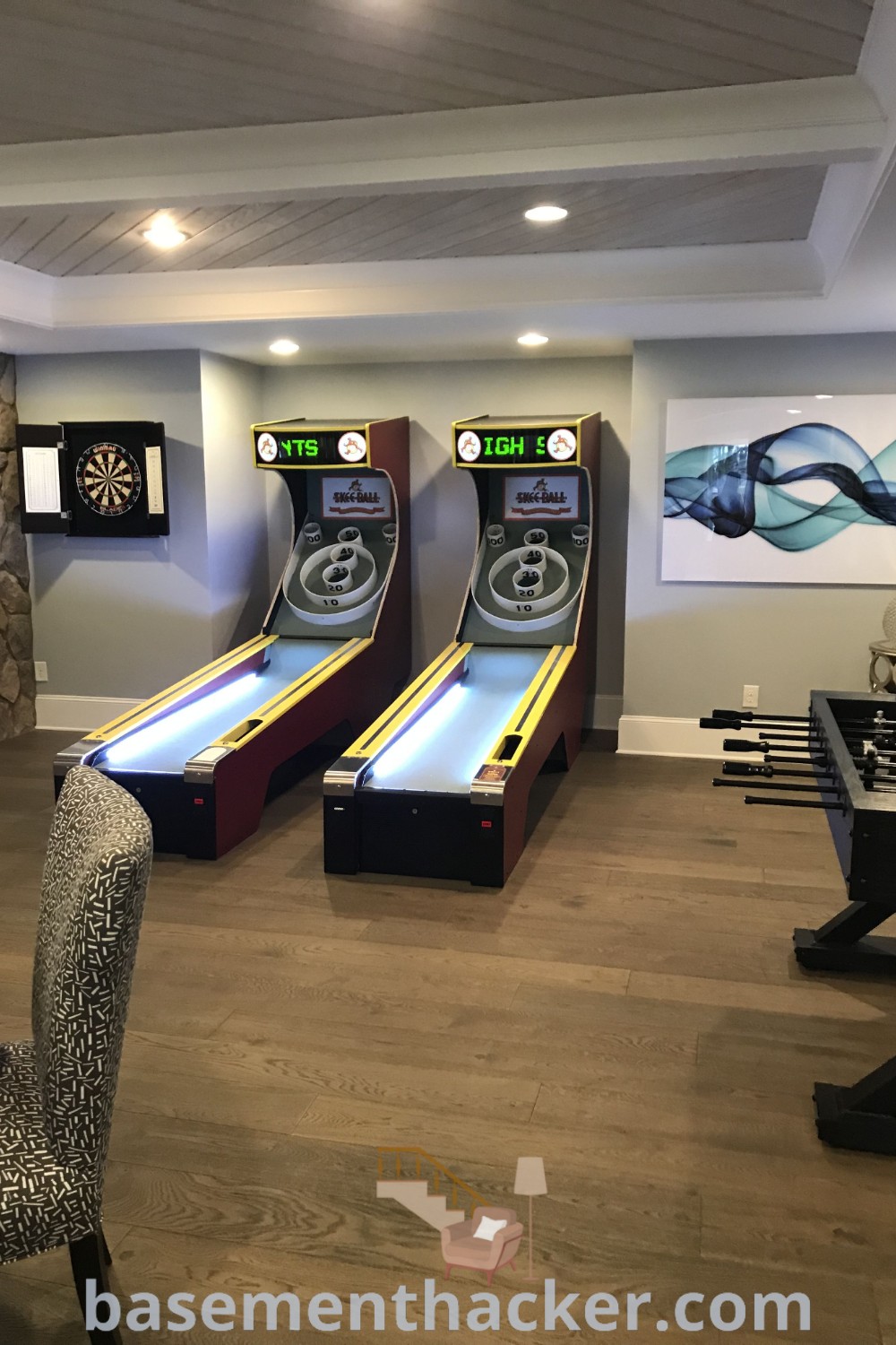A game room with two bowling machines and chairs, showcasing innovative design ideas for the ultimate entertaining space. This stylish bonus room design offers a cozy environment for gatherings and family fun. Explore more at basementhacker.com.