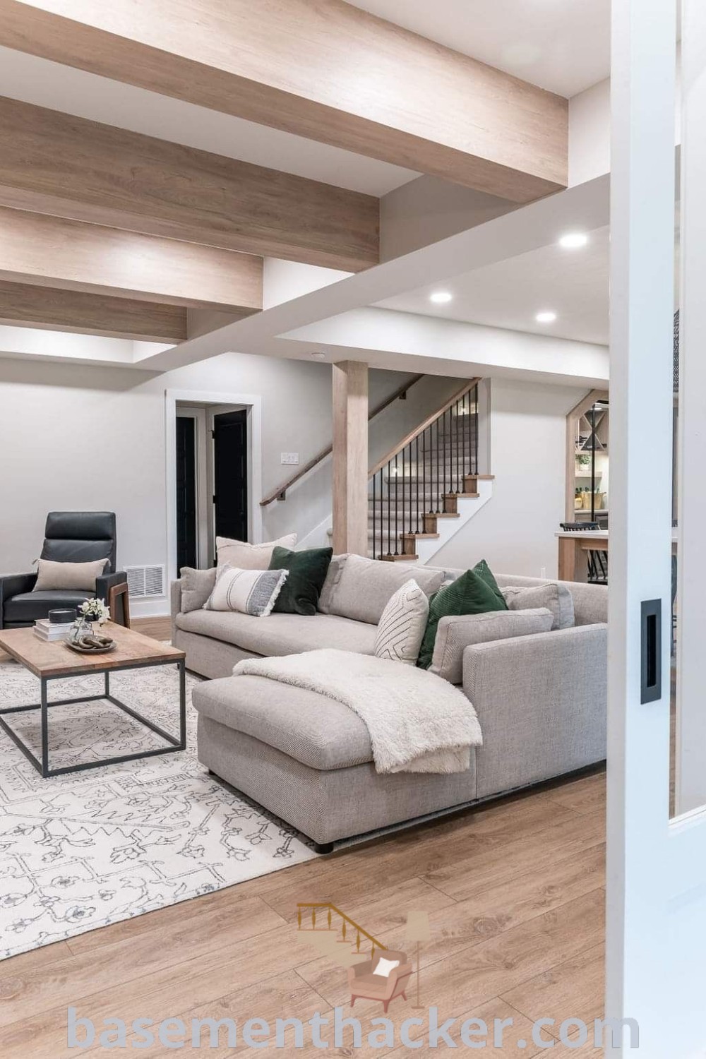 A modern basement living room with white walls and wood floors, showcasing stylish decor and innovative ideas for designing an inviting space. This basement layout inspires ultimate entertaining and cozy family time, offering the best basement remodeling ideas for your home. Visit basementhacker.com for more design inspirations.