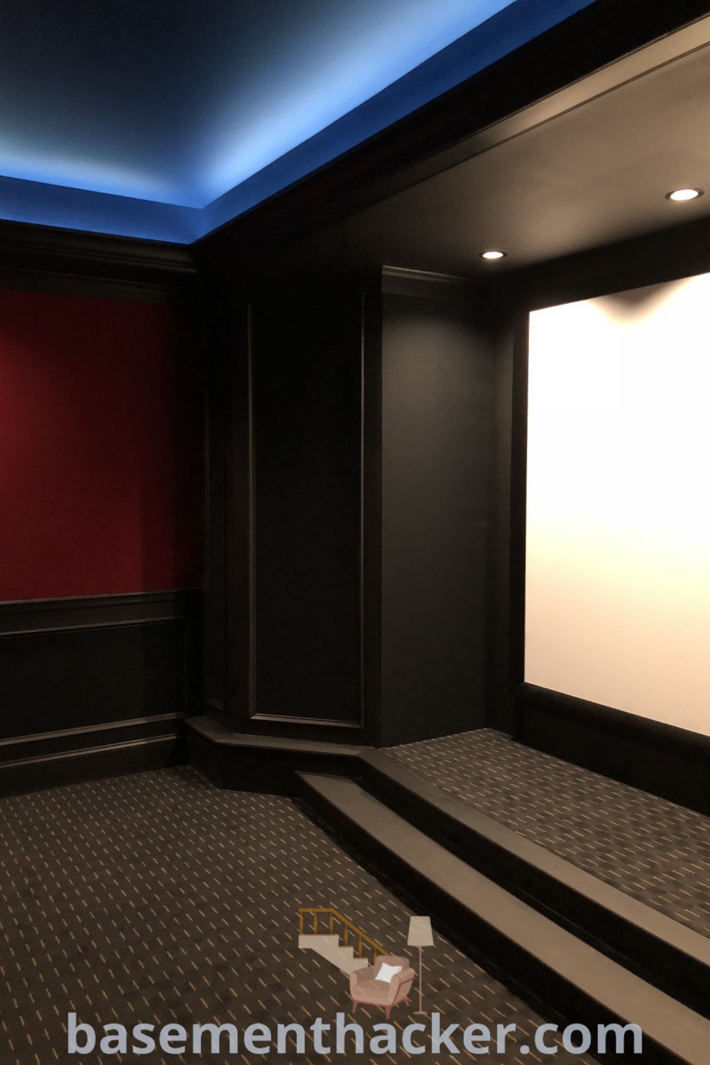 An empty theater room designed for ultimate entertaining, featuring steps leading to the screen. This cinema room design offers innovative ideas for stylish and functional home theaters, making it great for family movie nights and basement makeovers. Find more inspiration at basementhacker.com.