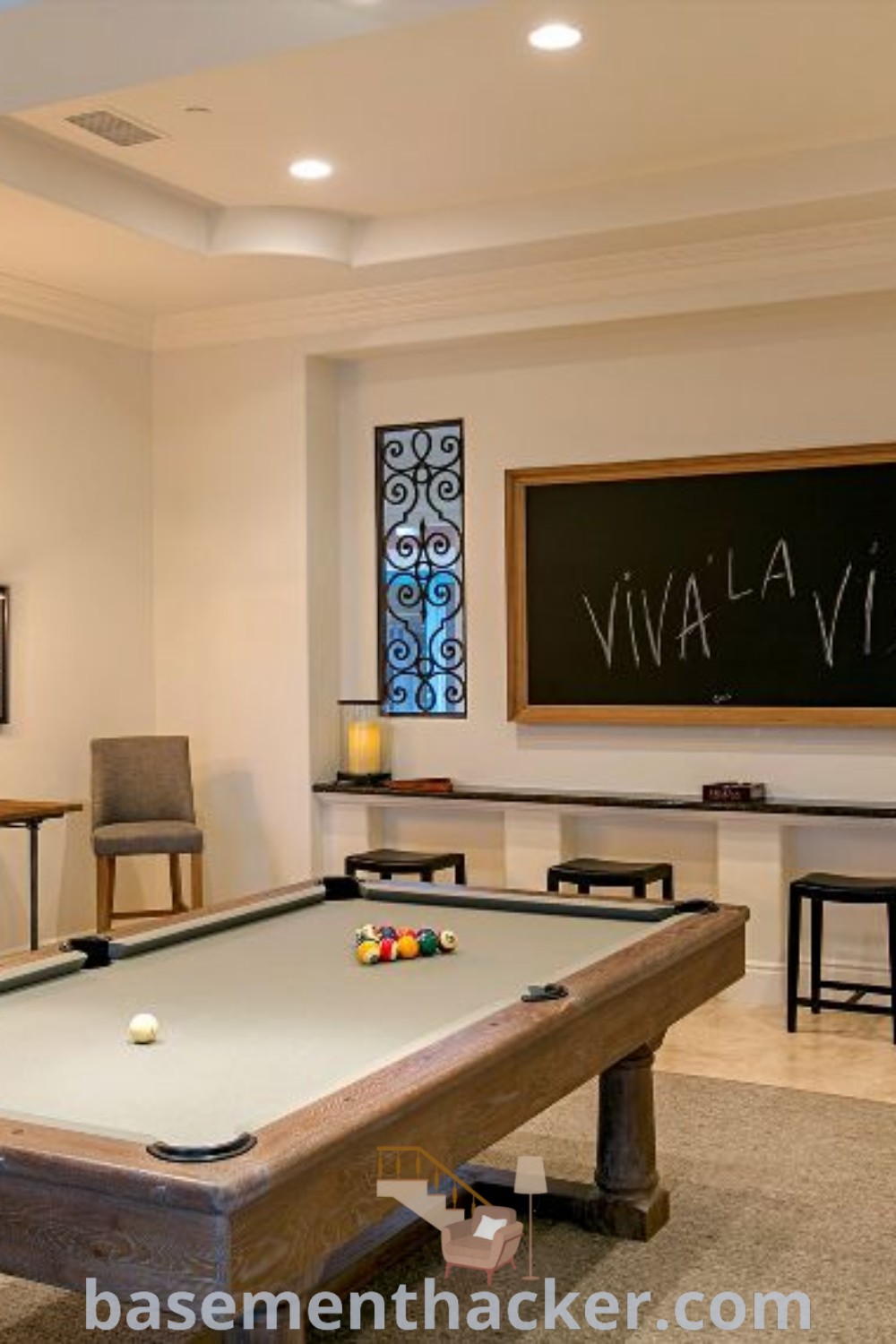 A stylish pool table room with a pool table, chairs, and a chalkboard on the wall behind it, showcasing innovative ideas for designing a cozy and functional entertainment space. This space reflects the best basement remodeling ideas for a family-friendly environment. Learn more at basementhacker.com.