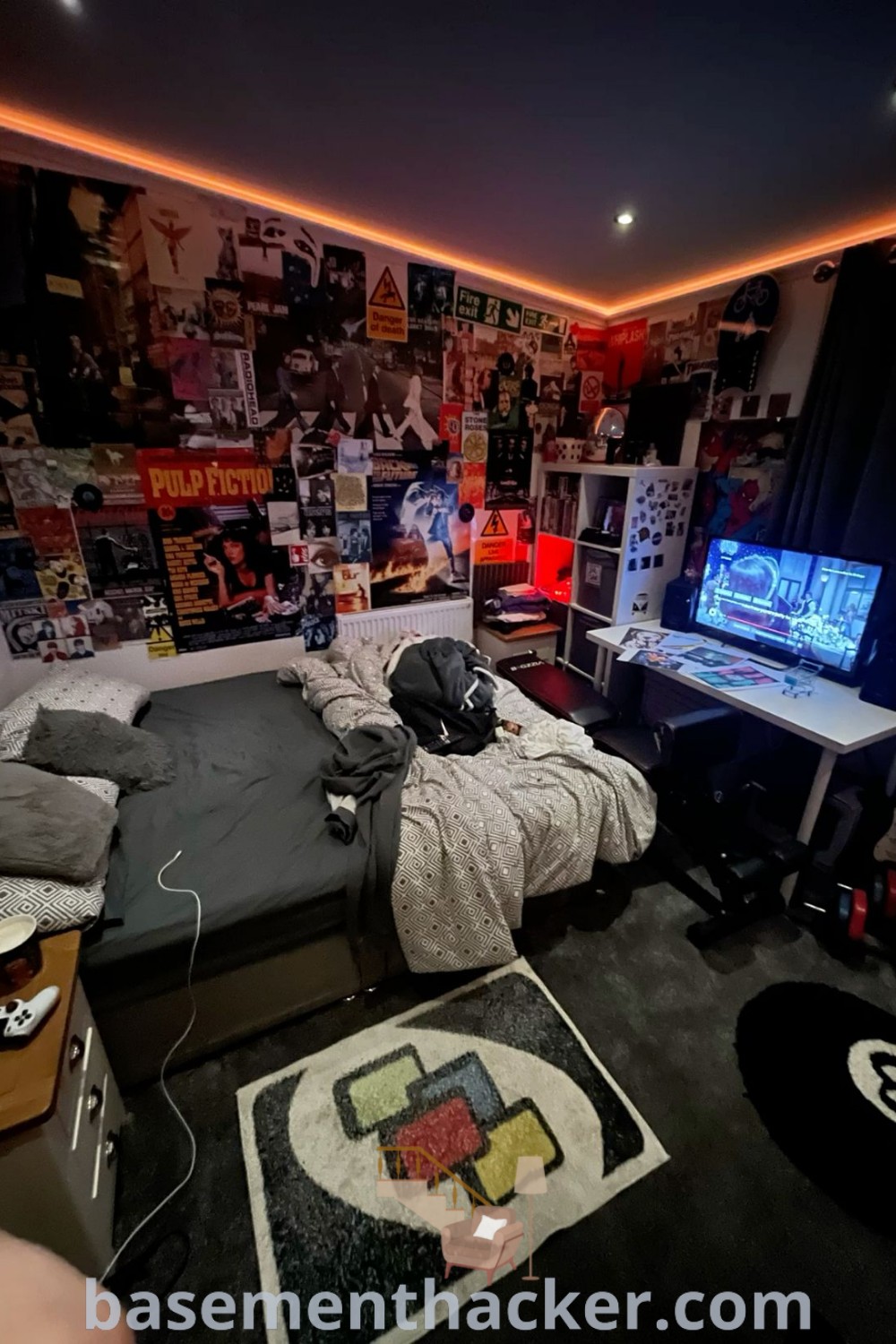 A stylish gaming apartment bedroom with a neatly made bed, a large screen TV, and a cozy seating area, showcasing innovative ideas for designing cool guy rooms. This aesthetic space is perfect for ultimate entertaining and offers decor inspiration for a cozy and organized home. Explore more stylish room ideas at basementhacker.com.