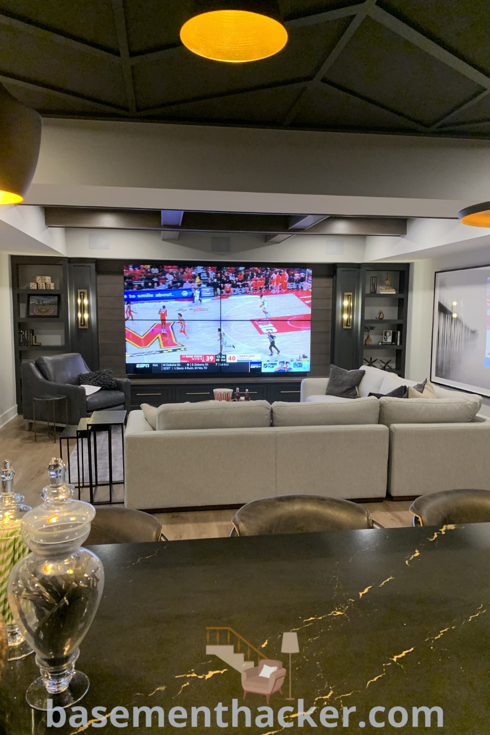 A beautifully designed basement living room with a flat-screen TV mounted above cozy furniture, showcasing innovative ideas for a stylish bonus space. Ideal for ultimate entertaining, this area reflects the best basement remodeling ideas for your home and offers a functional atmosphere for family enjoyment. Discover more at basementhacker.com.