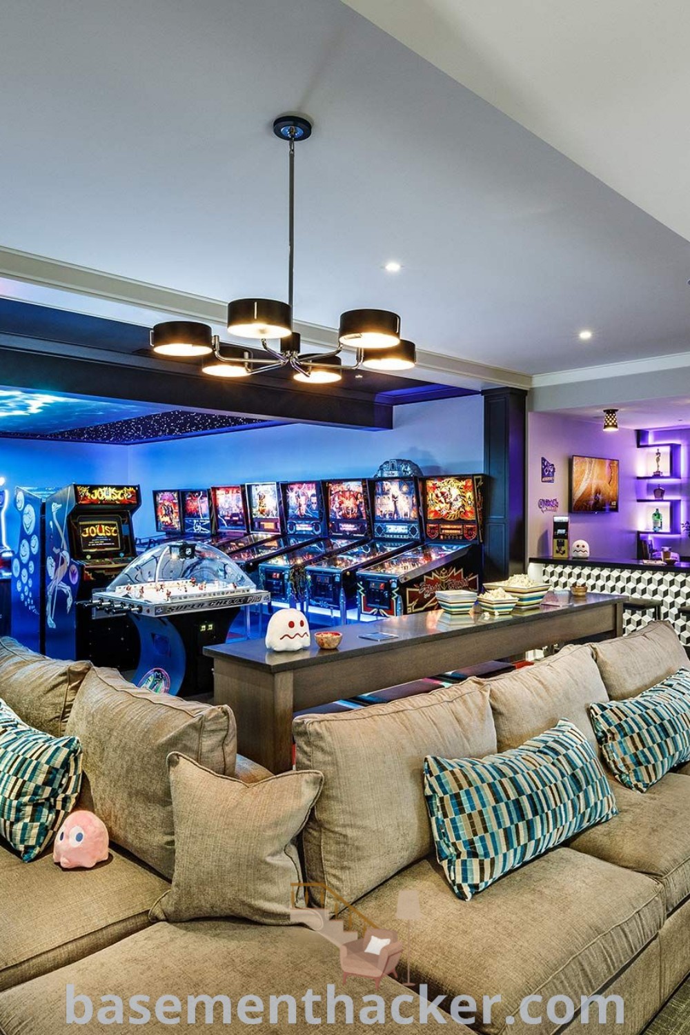 A stylish living room featuring various arcade machines and casino slot machines, surrounded by comfortable furniture. This home game room design offers innovative ideas for designing a game room basement, making it a perfect space for family fun and entertaining. Explore more inspiration at basementhacker.com.