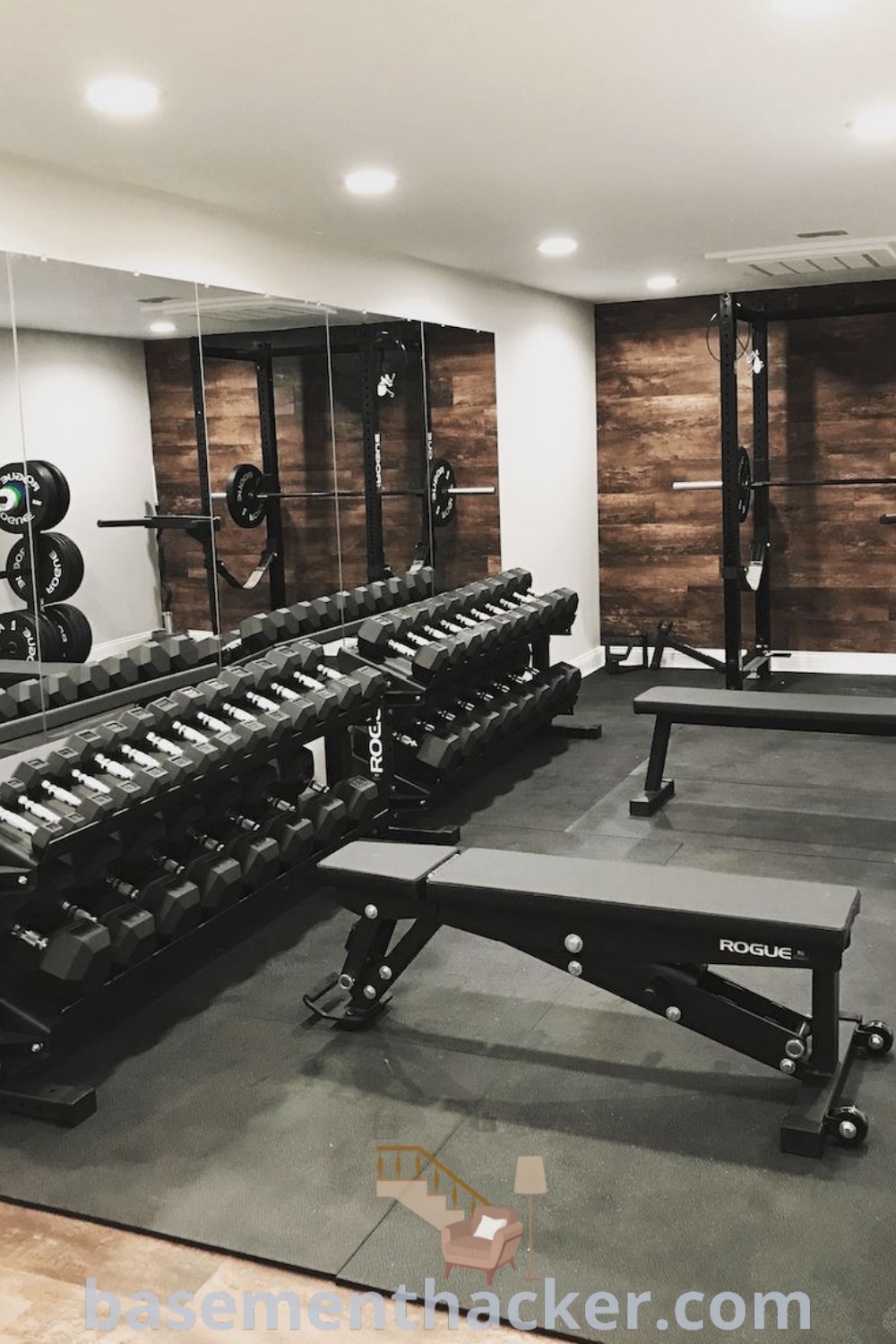 An empty home gym basement showcasing benches and weight machines along the wall, with mirrors reflecting the space. Perfect for innovative ideas for designing garage gyms, this setup offers functional benefits and aesthetic appeal for your ultimate entertaining or workout room. Discover more home gym inspirations at basementhacker.com.