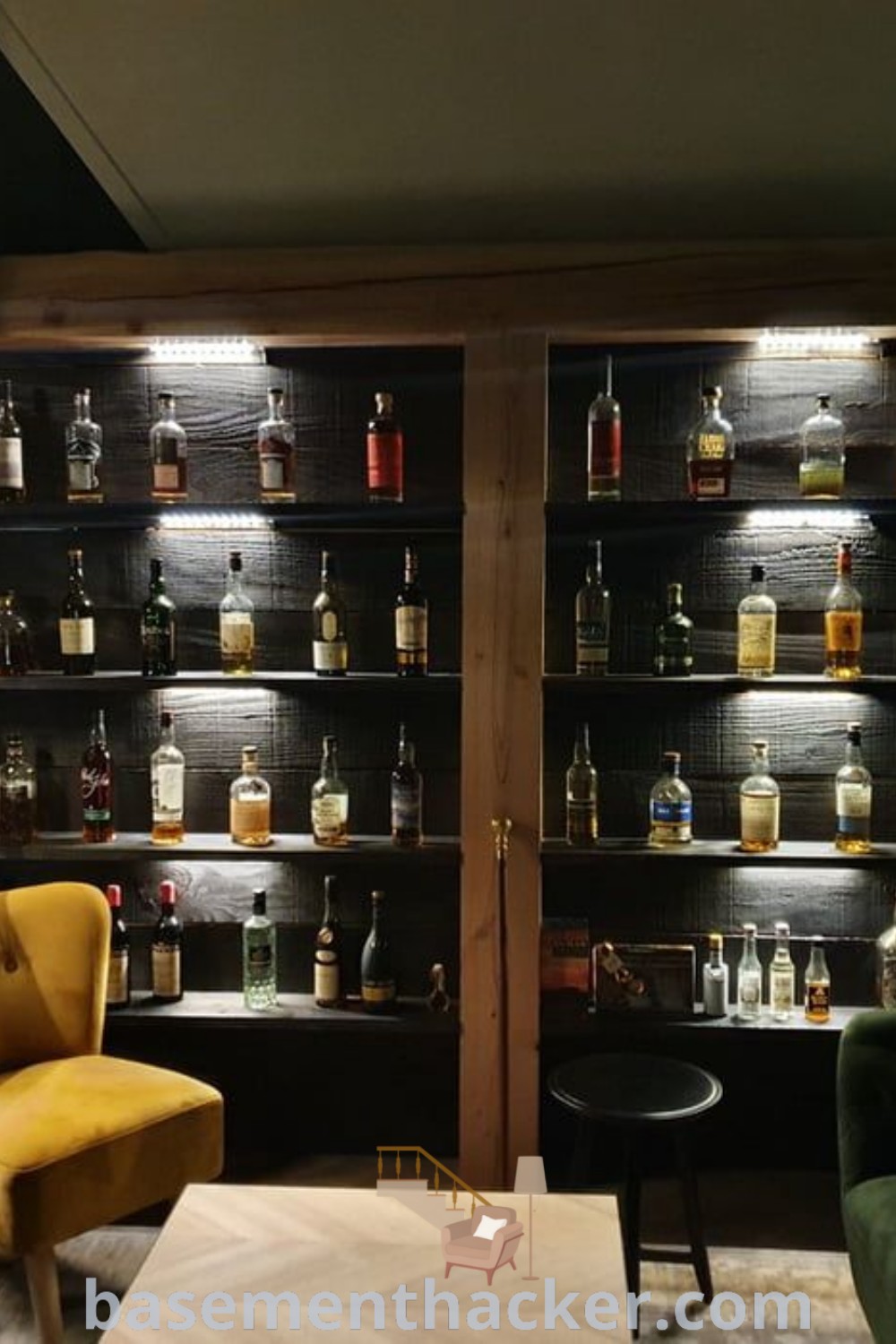 A cozy whiskey lounge filled with numerous bottles on shelves next to a stylish chair and table, ideal for home bar plans and bourbon tasting. This design offers innovative ideas for a stunning basement makeover, perfect for entertaining guests. Find more creative inspiration at basementhacker.com.
