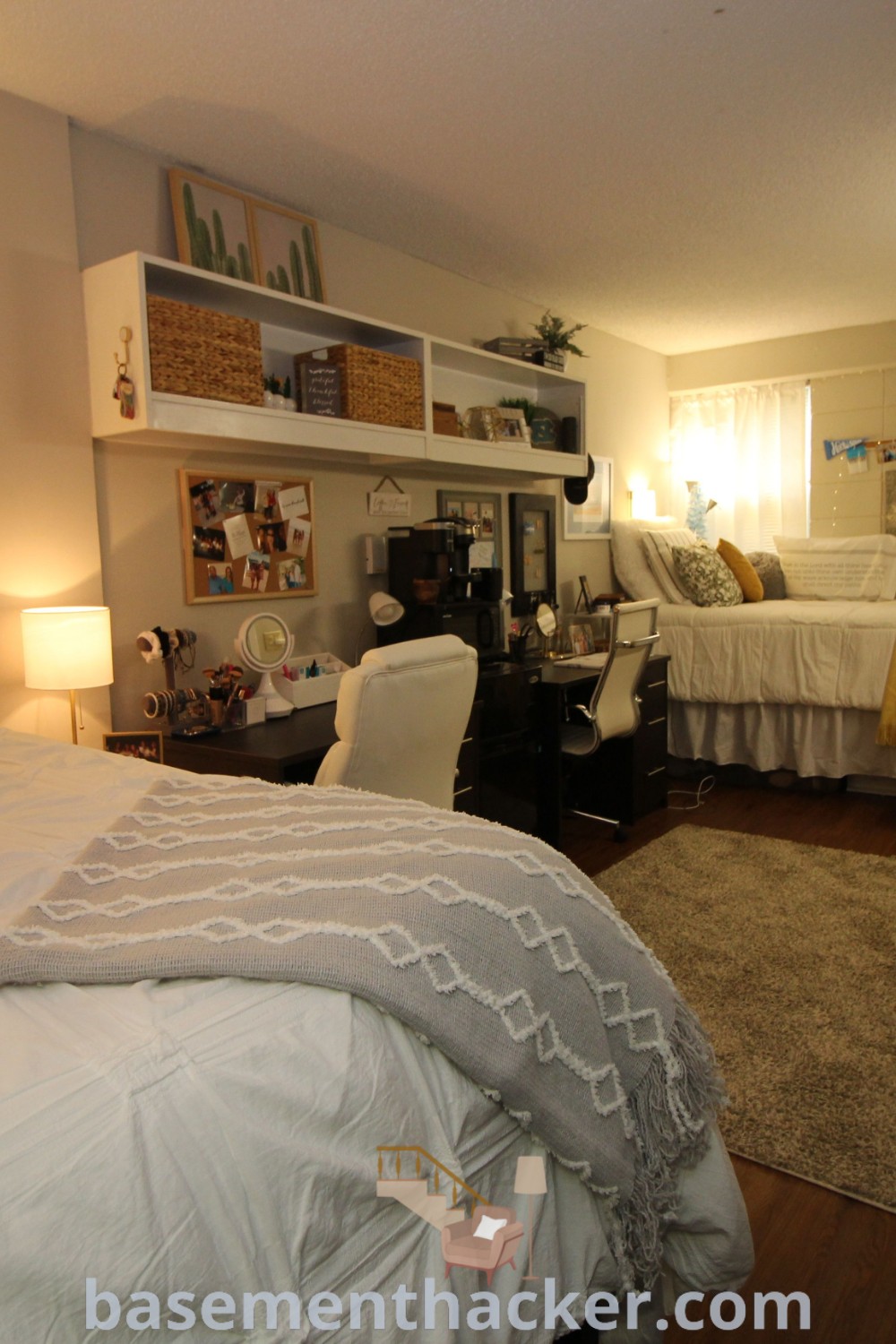 A stylish college dorm room with a neatly made bed, TV on a stand, and two lamps, demonstrating innovative ideas for a cozy and functional student space. This design reflects the best dorm room layouts and hacks for a stylish bonus room, perfect for relaxing and entertaining. Discover more on basementhacker.com.