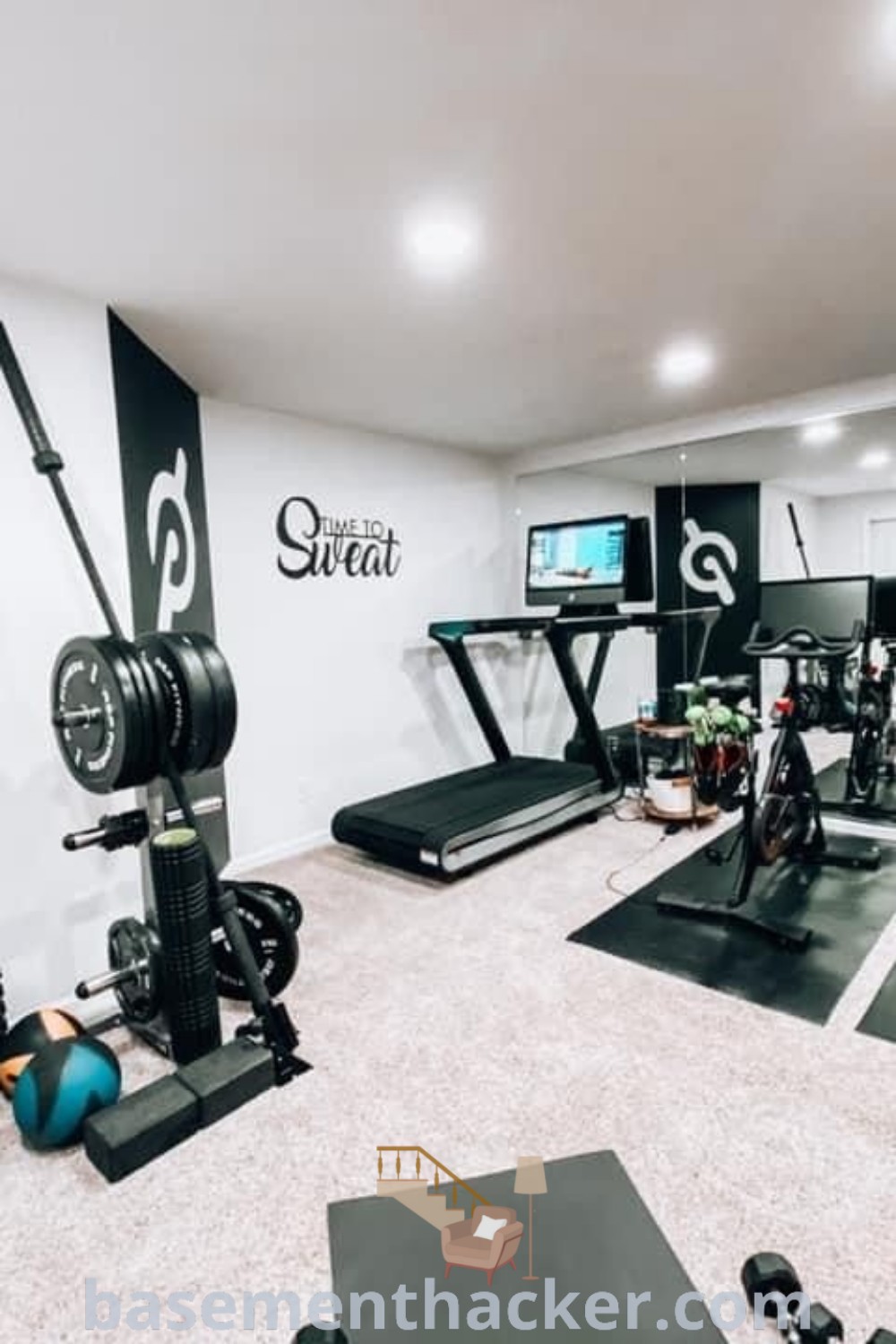 A man standing in a modern home gym setup featuring various exercise equipment, showcasing innovative gym room decor ideas including a basement gym area and stylish workout room flooring. This exercise room blends functionality with aesthetic appeal, perfect for anyone seeking to create a cozy and organized fitness space. Find more design tips at basementhacker.com.