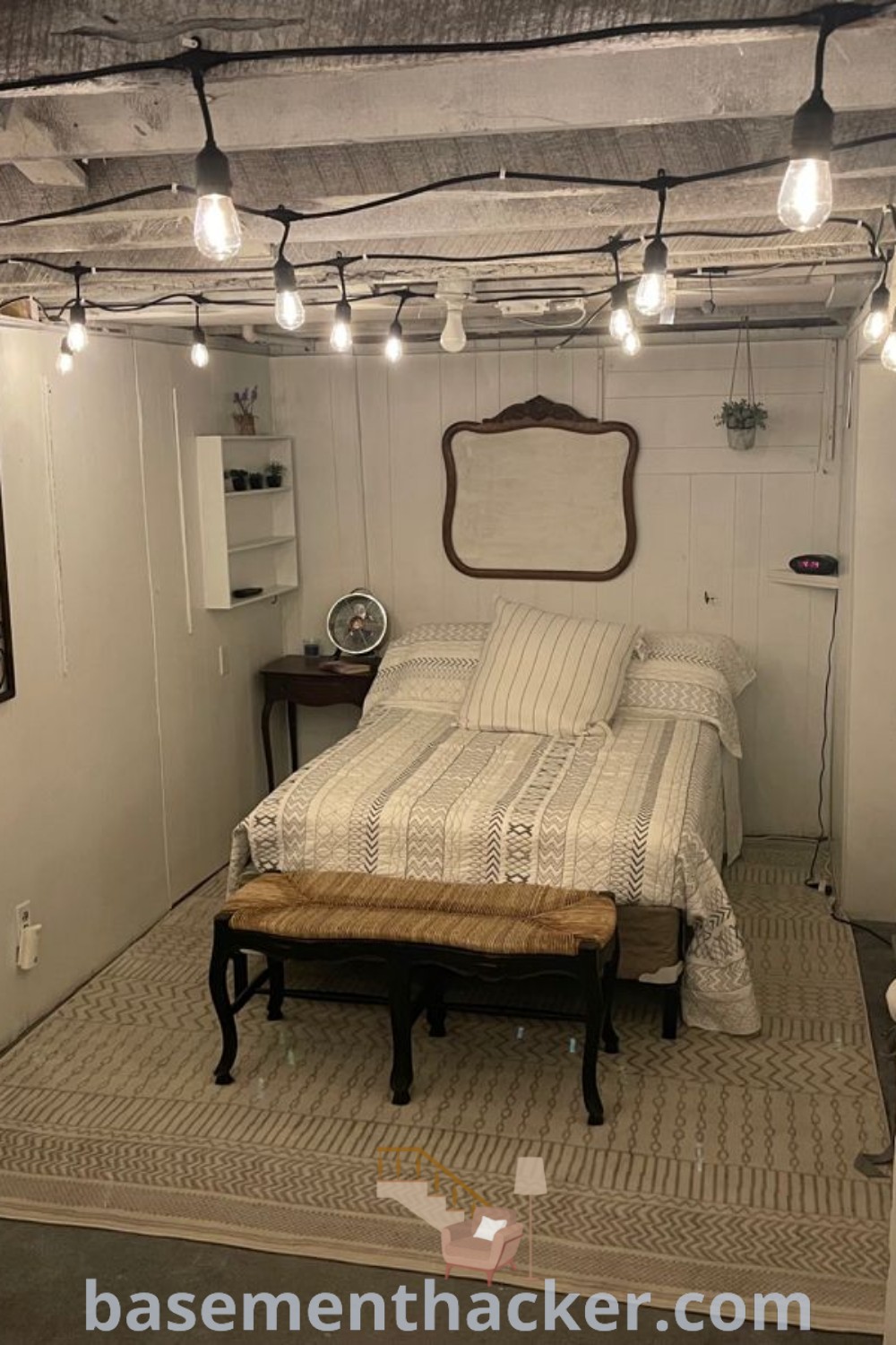 A cozy basement bedroom with a comfortable bed, a wall-mounted air conditioner, and a ceiling fan, showcasing innovative ideas for designing an inviting space. Discover basement remodel ideas and stylish bonus room design concepts at basementhacker.com.