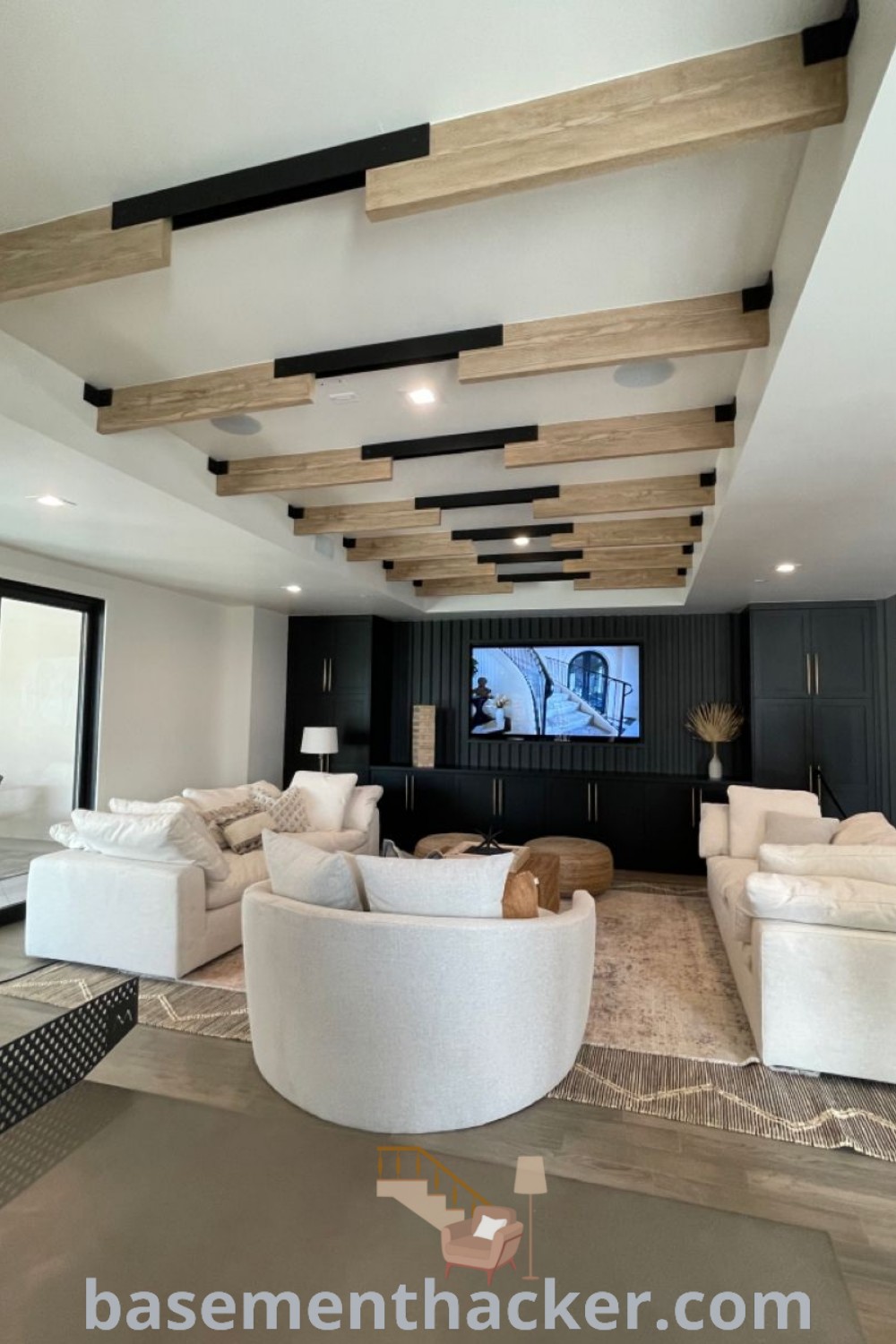 A modern living room in a stylish basement filled with contemporary furniture and a flat screen TV mounted on a white exposed ceiling, showcasing innovative ideas for designing a cozy bonus space. Explore more awesome basement makeovers at basementhacker.com.