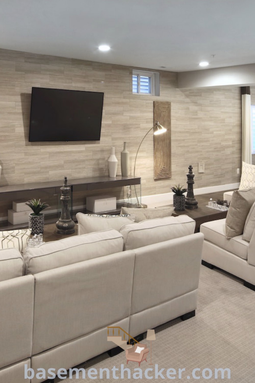 A cozy basement living room filled with furniture, a flat screen TV mounted above a fireplace, showcasing innovative ideas for designing a stylish and functional space. Discover more awesome basement makeover ideas for ultimate entertaining at basementhacker.com.