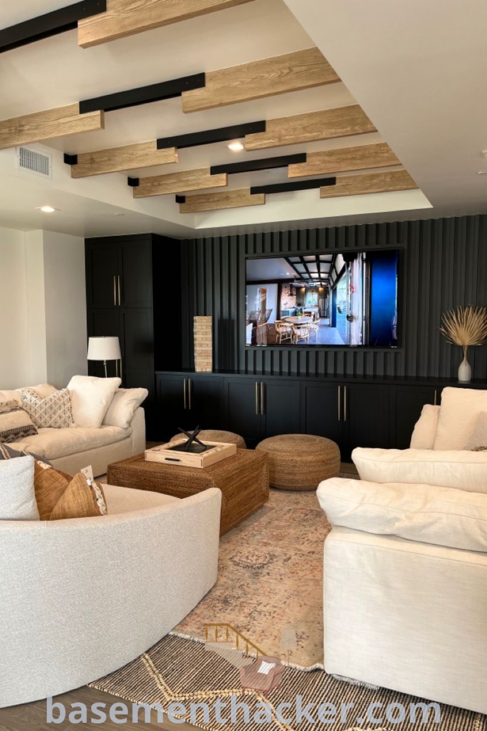 A cozy black and white entertainment room with a flat screen TV mounted above a stylish sectional, ideal for family movie nights or game room layouts. This image showcases innovative basement makeover ideas for a functional and stylish home space. Explore more design inspirations at basementhacker.com.