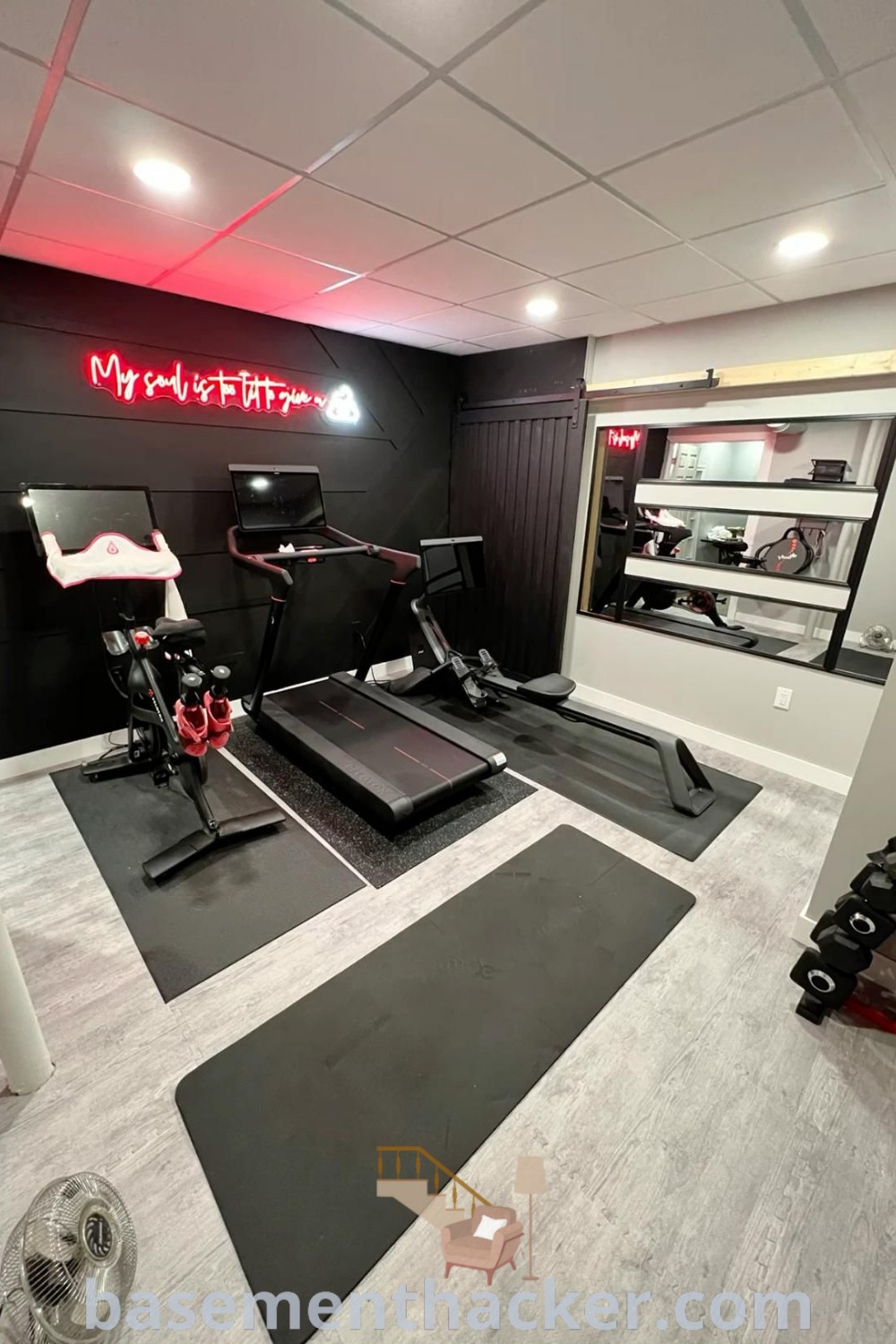 A stylish home gym setup that includes a Peloton rowing machine and a treadmill, designed for ultimate entertaining and fitness activities. This gym in the basement features innovative ideas for a functional and aesthetic home gym that the whole family will enjoy. Discover more at basementhacker.com.