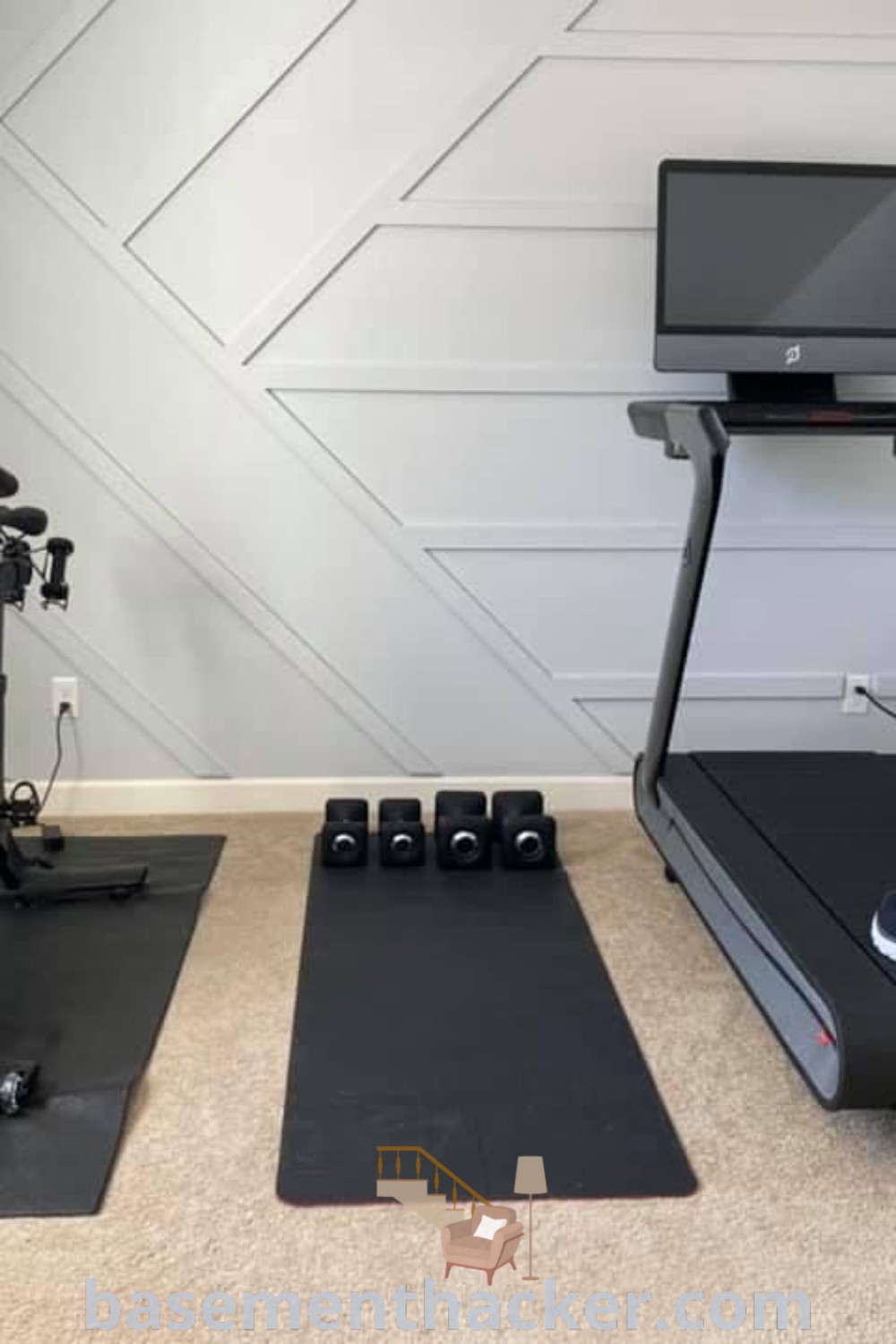 A home gym in a small bedroom featuring treadmills, exercise mats, and a computer monitor on the wall, exemplifying stylish home gym ideas for basement workout rooms. This design combines innovation with functionality, offering the best basement remodeling ideas for creating an organized and cozy workout space. For more inspiration, visit basementhacker.com.