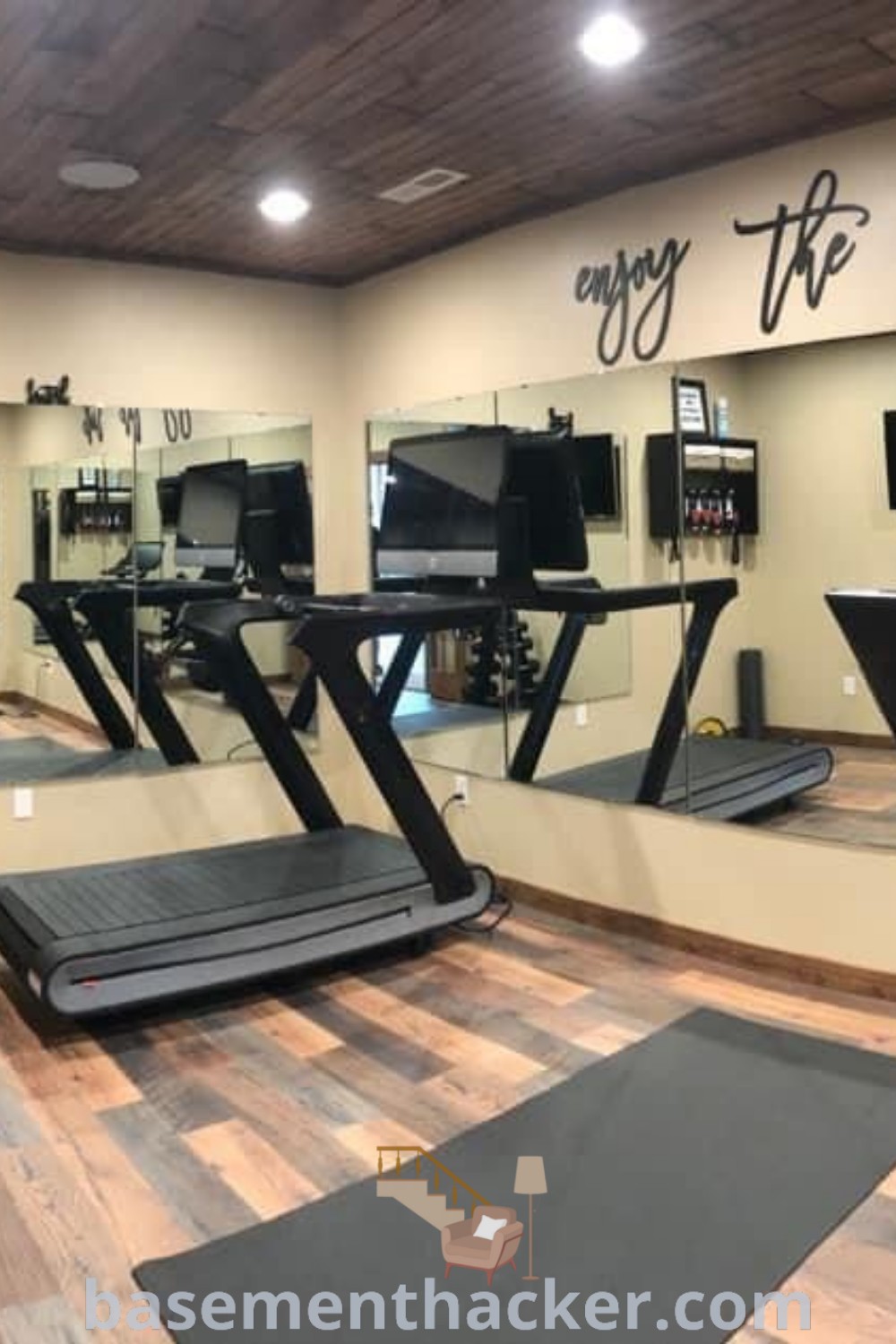 A well-designed gym in a basement featuring treadmills, exercise bikes, and mirrors. This space showcases innovative ideas for designing a multipurpose basement gym and serves as a stylish bonus room for family use. Find more gym room ideas at basementhacker.com.