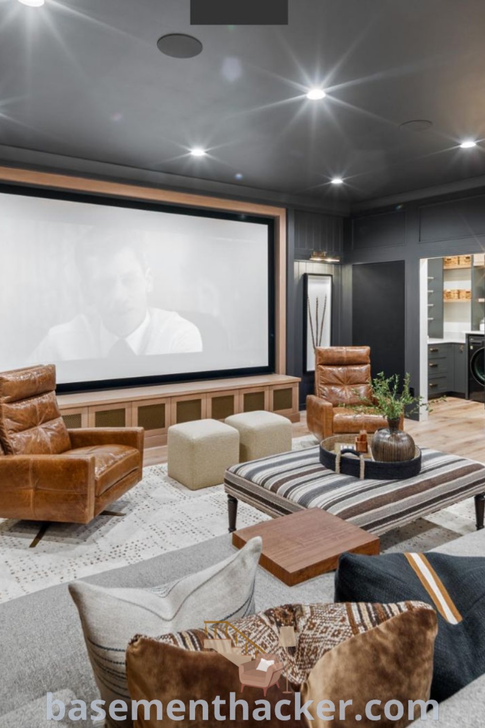 A large living room with couches, chairs, and a projector screen, designed as a contemporary movie room and family play area. This modern rec room offers innovative ideas for stylish and functional basement makeovers, ideal for family entertaining. Discover more at basementhacker.com.