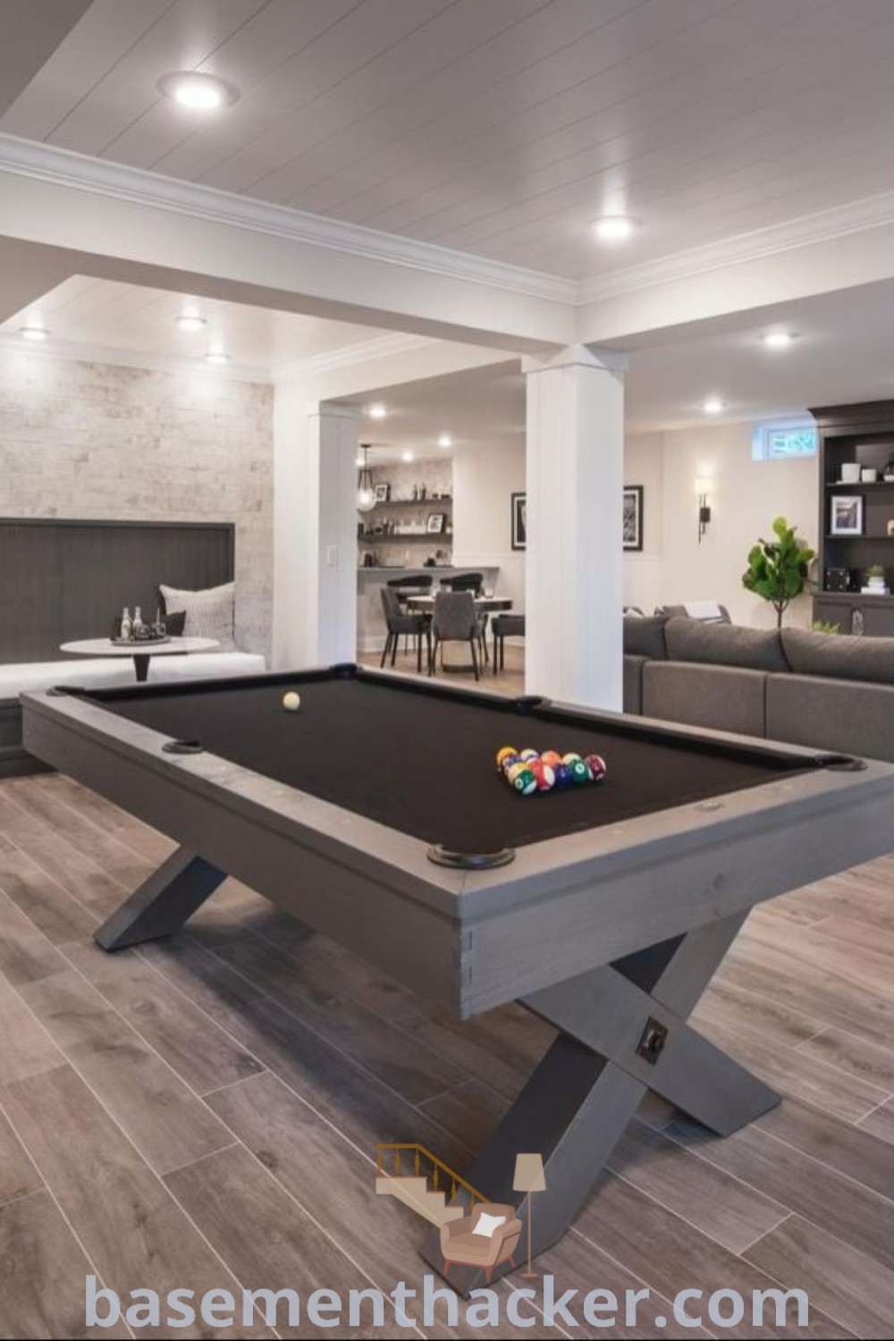 A modern black interior design featuring a pool table in the middle of a living room, emphasizing stylish bonus room design ideas for families. This black basement layout includes a chic home bar, offering innovative ideas for a cozy and organized entertainment space, perfect for game night. Explore more inspiration at basementhacker.com.