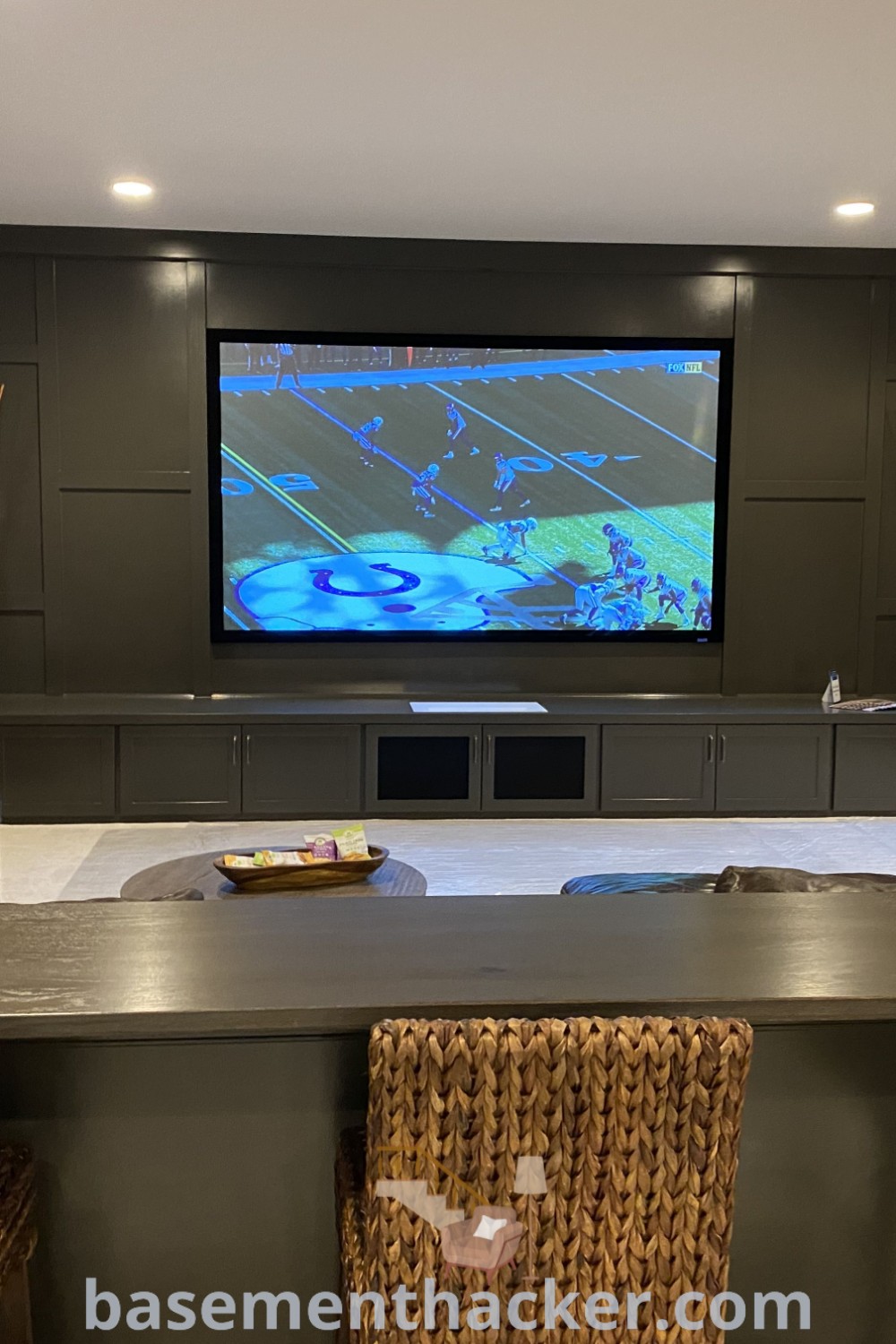 A stylish living room filled with furniture, featuring a flat-screen TV on the wall, a built-in bar behind the couch, perfect for basement entertainment room ideas. This space highlights innovative design ideas for a family game room and kids hangout room, ensuring a cozy and organized home. Discover more inspiring basement remodeling ideas at basementhacker.com.