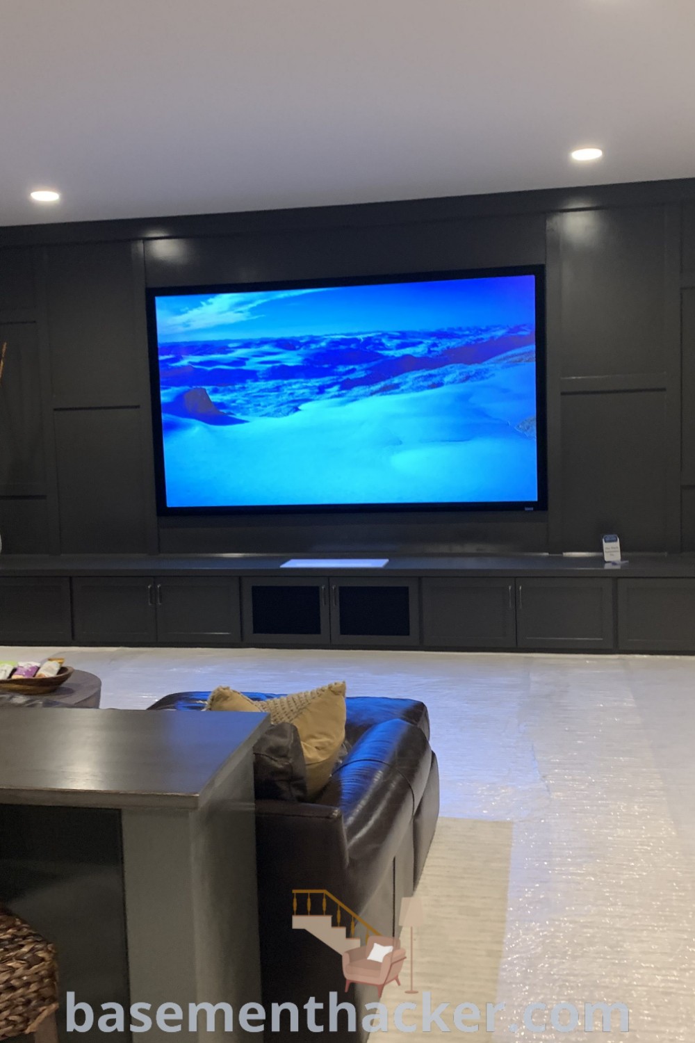 A living room in a basement filled with furniture and a flat-screen TV mounted on the wall, showcasing stylish decor and innovative basement makeover ideas for a cozy and organized home. Explore more family-friendly basement living room ideas at basementhacker.com.