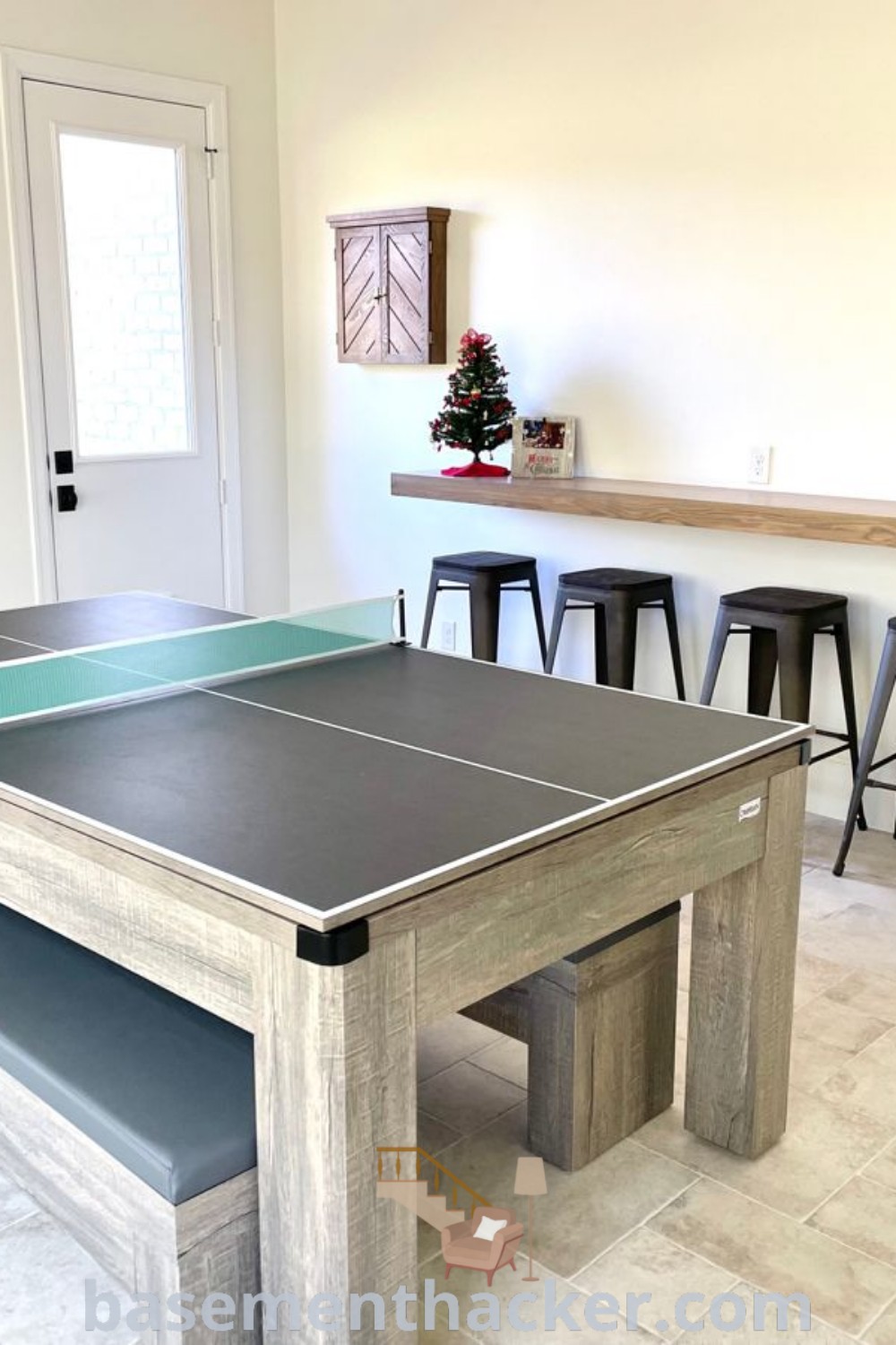A ping pong table in a stylish game room with stools and a bar, designed for ultimate entertaining. This basement ping pong setup showcases innovative ideas for a functional family space, incorporating elements from backyard games to inspire cozy and organized home design. Explore more at basementhacker.com.