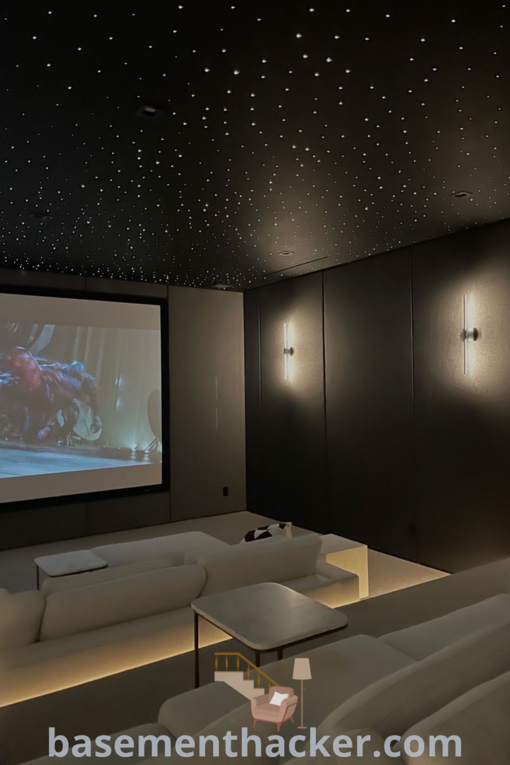 A large white couch in a home cinema room decorated with a projector screen and a starry ceiling. This stylish space embodies the latest cinema room aesthetic trends, providing innovative ideas for designing a cozy and functional entertaining area. For more decoration tips, visit basementhacker.com.