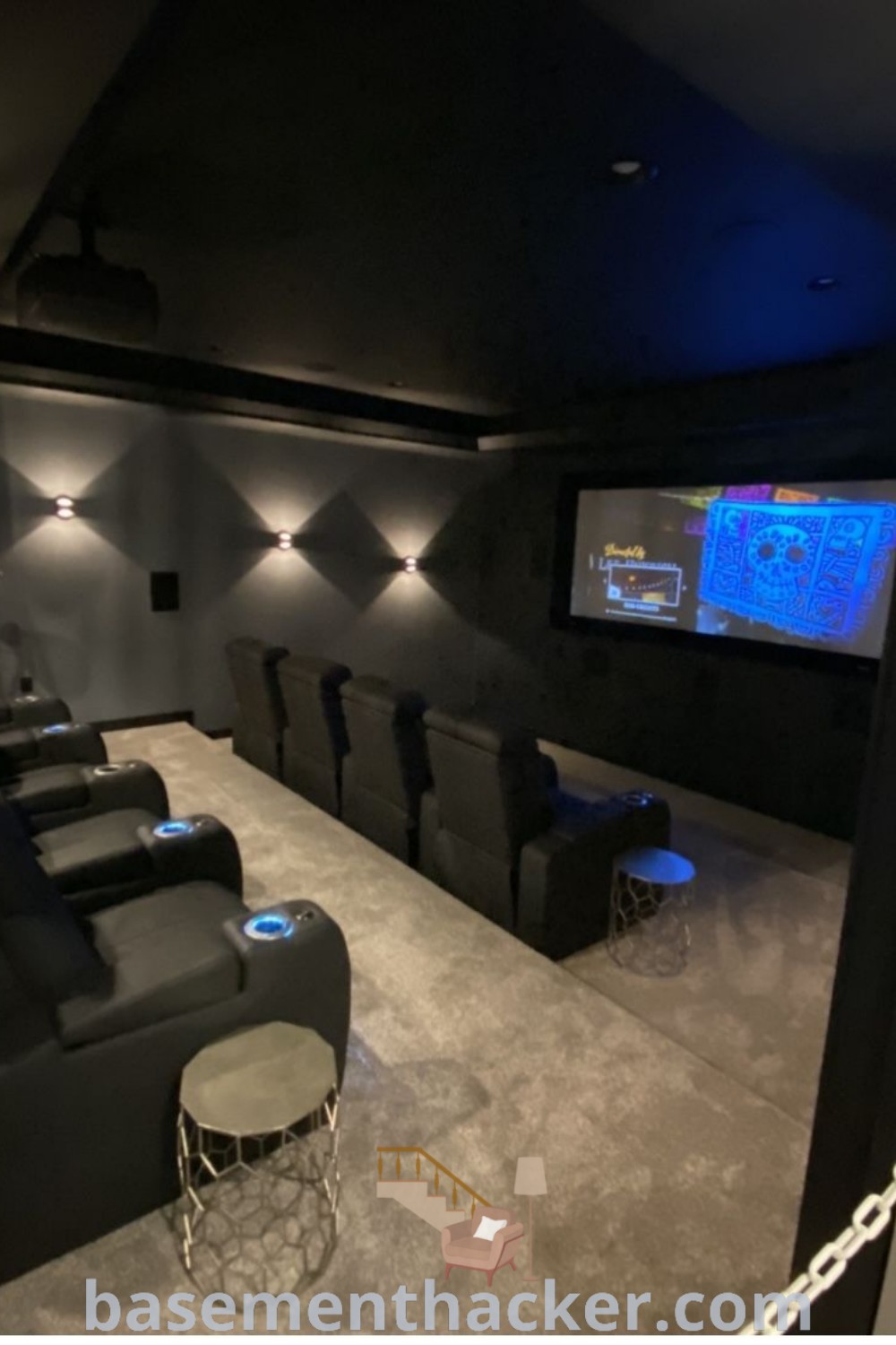 A cozy home theater with black leather seats, blue lights on the wall, and two stools, showcasing innovative ideas for designing a stylish and functional home theater room. Perfect for remodeling, this setup offers stylish bonus room design ideas for families, ensuring entertainment for all. Explore more on basementhacker.com.