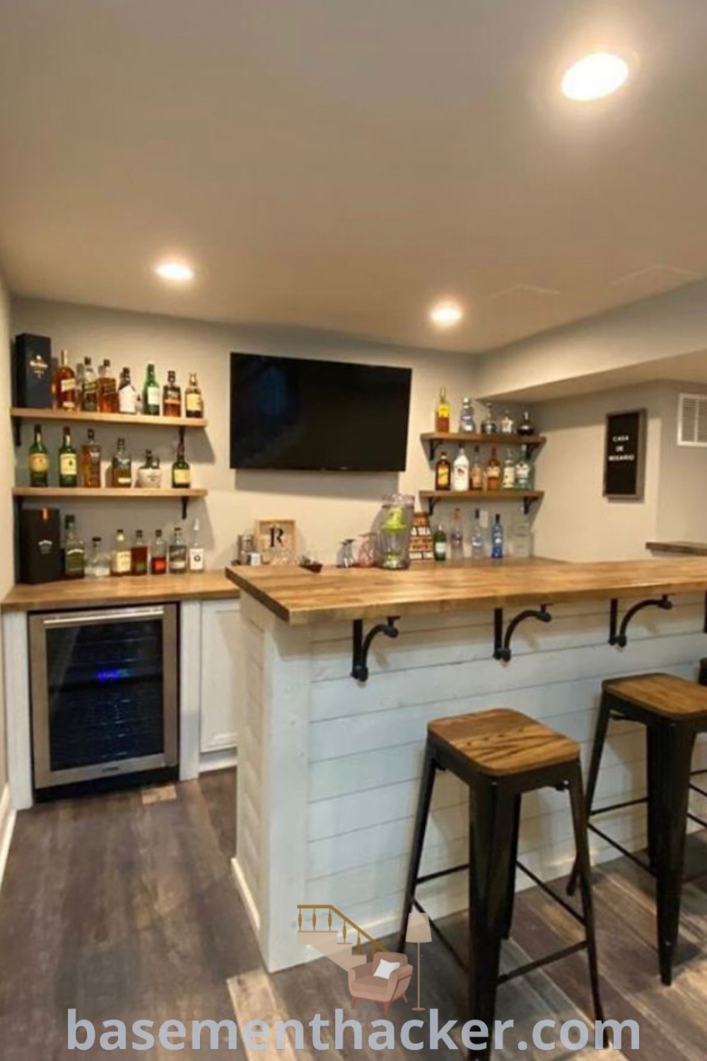 A stylish home bar featuring stools in the center, designed for ultimate entertaining in a finished basement. This innovative makeover showcases ideas for a cozy and organized space, including budget-friendly options for small basement bars. Discover more about basement remodeling at basementhacker.com.