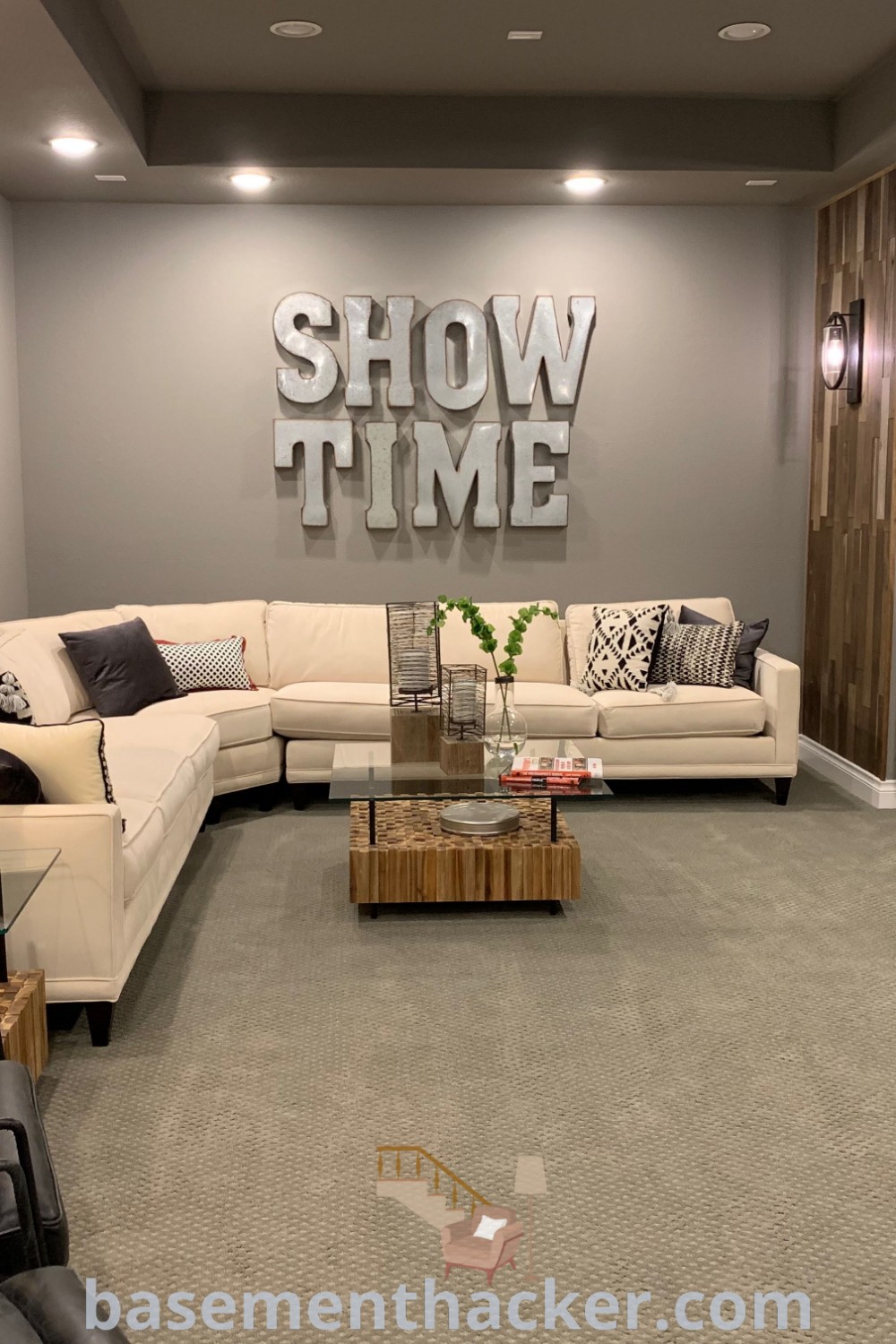 A modern game room with a sectional sofa, flat-screen TV mounted on the wall, and stylish decor, perfect for innovative basement makeovers. This space showcases ideas for a stylish and functional home design from basementhacker.com, ideal for family gatherings and entertainment.