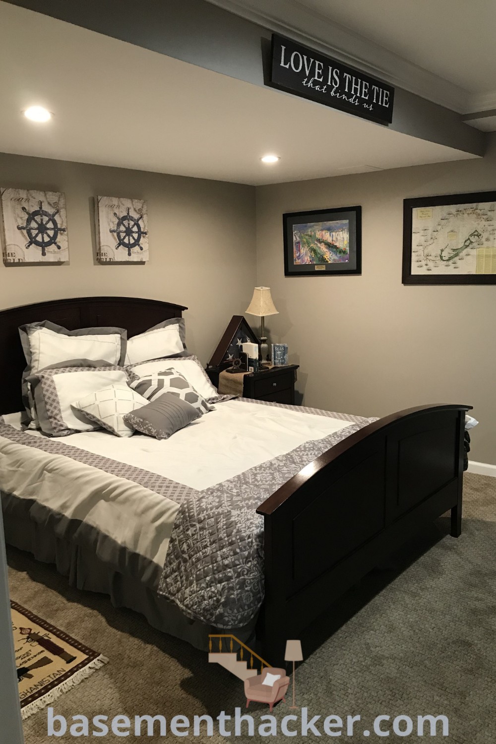 A cozy basement bedroom with a bed and two pictures that say "love is here" on the wall, showcasing innovative basement makeover ideas for stylish and functional home design. This space offers inspiration for finished basement bedroom ideas and stylish bonus room design ideas for families. For more unique decor suggestions, visit basementhacker.com.