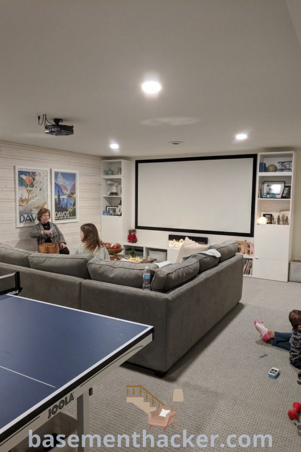 Two children sitting on the floor in a cozy hangout room with a ping pong paddle in front of a fun table, ideal for creating a stylish and functional home design. This basement game room offers innovative ideas for families, perfect for remodeling and enhancing your space. Explore more creative inspirations at basementhacker.com.