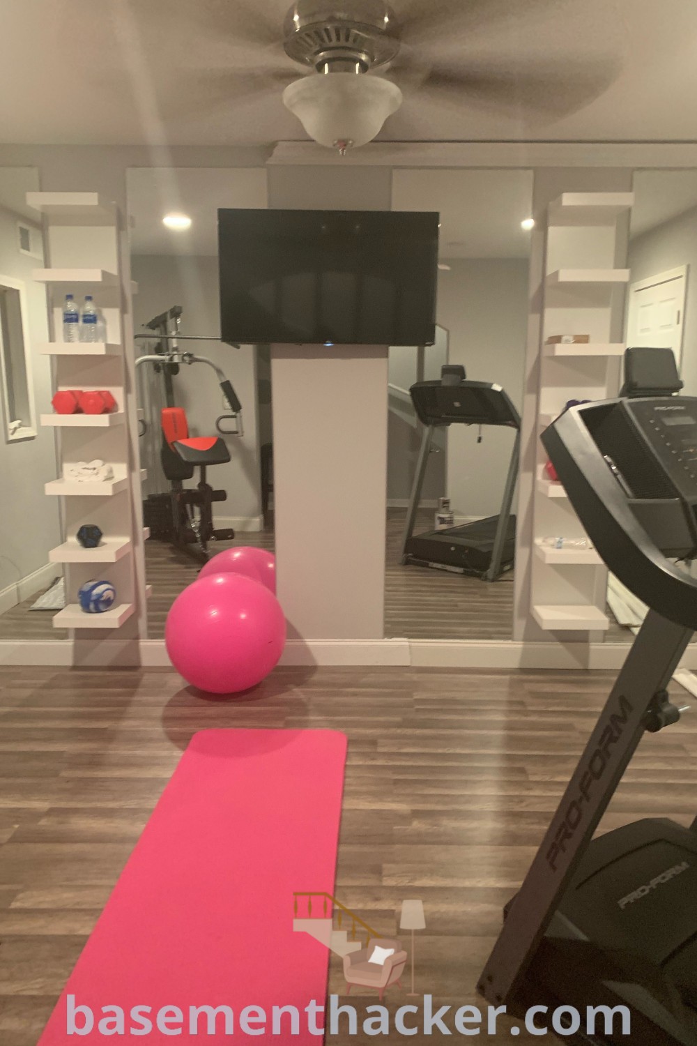 A modern exercise room in a basement setup, showcasing treadmills and a bright pink yoga mat, designed for ultimate fitness. This stylish fitness area offers innovative ideas for a cozy and organized home, making it a functional space for all family members. Discover more remodeling inspiration at basementhacker.com.