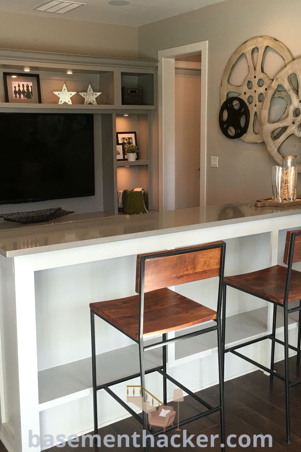 A modern basement bar with four stools and a television mounted on the wall creates a stylish and functional space for entertaining and relaxing. This design showcases innovative basement makeover ideas perfect for family media rooms and small basement living rooms, providing inspiration for a stylish and organized home. For more decor tips, visit basementhacker.com.