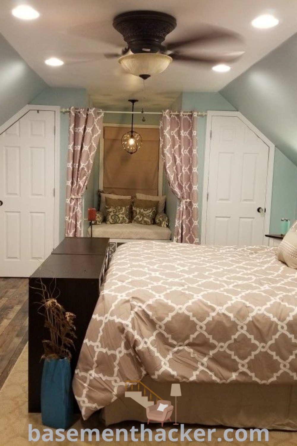 A cozy attic bedroom with blue walls and wooden floors, designed with a sloped ceiling that enhances the charm. This innovative bedroom layout offers stylish ideas for a master suite, perfect for remodeling and creating a comfortable living space. Explore more tips at basementhacker.com.