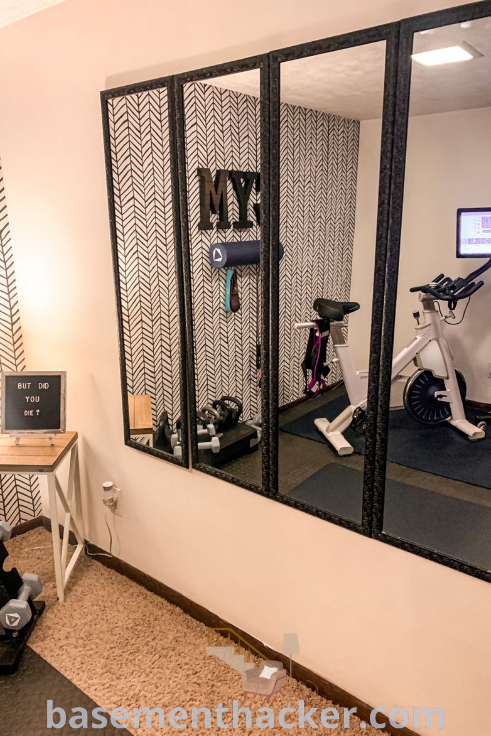 A stylish home gym with exercise equipment and a bike positioned in front of mirrors on the wall, showcasing innovative ideas for a cozy and functional fitness room. This setup offers decor inspiration for garage gym spaces and at-home workout gym ideas. Discover more innovative basement makeover ideas and tips at basementhacker.com.
