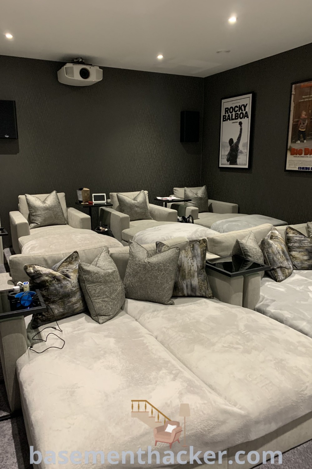 A beautiful living room filled with white couches and a wall-mounted movie projector, representing stylish home cinema room ideas. This design showcases innovative cinema room aesthetics, ideal for ultimate entertaining and family enjoyment. Discover more at basementhacker.com.