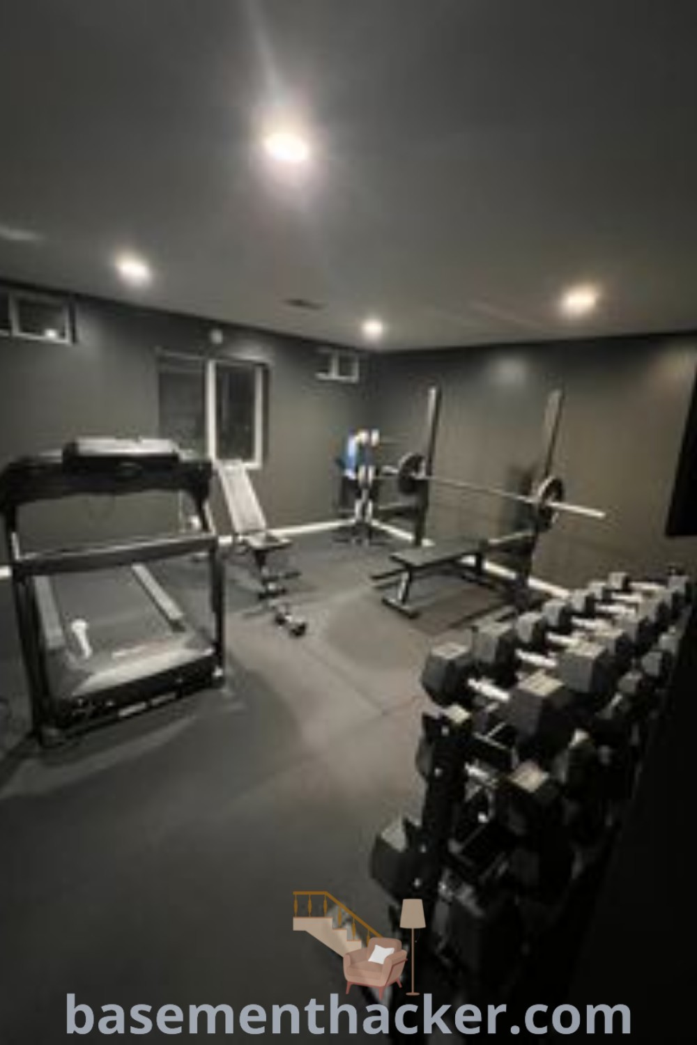 An empty gym with rows of sleek exercise equipment, showcasing a modern black home gym aesthetic with dark walls. This innovative basement makeover idea provides functional design elements for an optimal workout experience. Explore more ideas for a stylish and organized home gym at basementhacker.com.