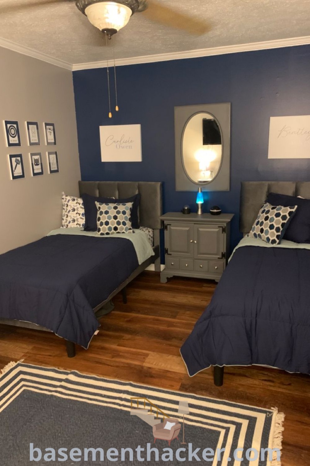 A boys bedroom with two beds, navy blue walls, wooden floors, and a rug, showcasing innovative ideas for a stylish and functional space. Discover more design inspiration at basementhacker.com.