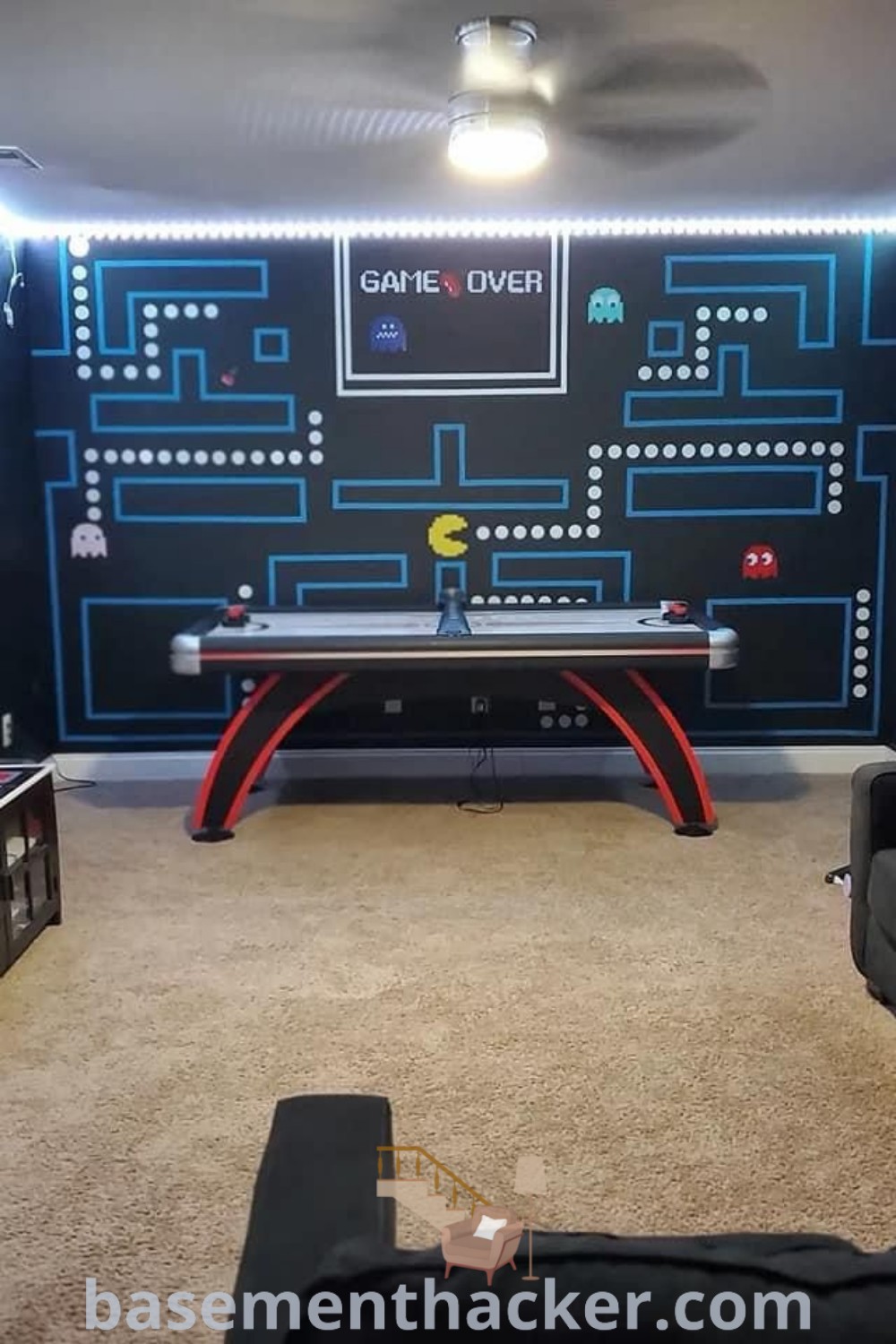 A stylish living room designed for a gaming experience with a large black video game wall, comfortable couches, and innovative furniture. This setup exemplifies game room ideas for ultimate entertaining, blending aesthetics and functionality perfectly. For more inspiration, visit basementhacker.com.