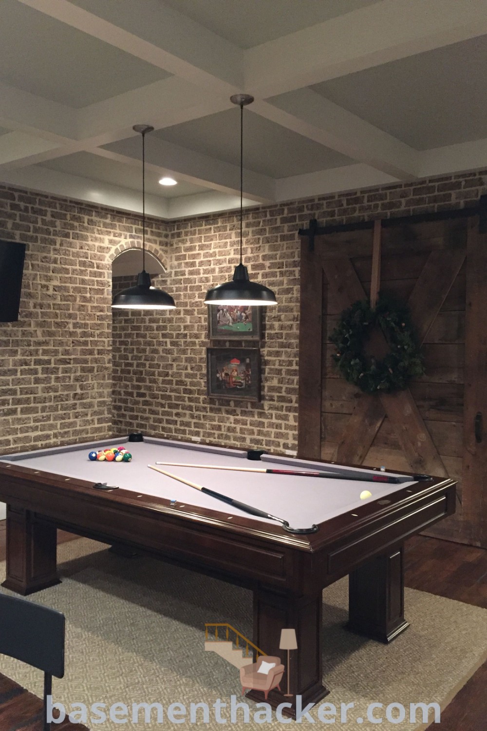 An industrial billiard room with a sleek pool table in the center, showcasing elements of a stylish man cave design. The room features modern fireplace ideas along with decor suited for ultimate entertaining and innovative game room aesthetics. For more inspiration, visit basementhacker.com.