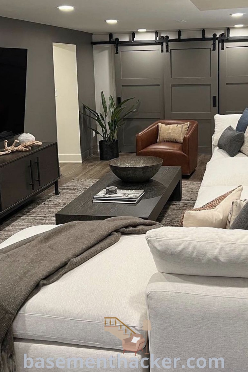 A cozy living room filled with furniture and a flat-screen TV in a small finished basement, showcasing innovative design ideas for ultimate entertaining. This space serves as a stylish bonus room design for families, offering inspiration for basement makeovers and remodeling at basementhacker.com.