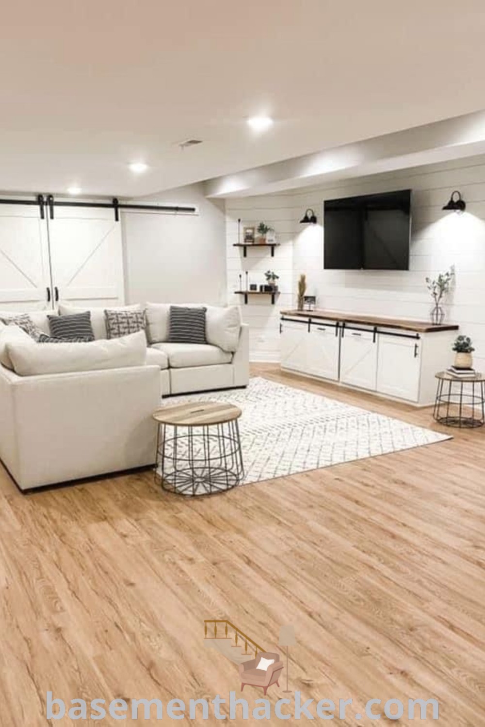 A beautiful living room in a finished basement showcasing a cozy floating couch, modern farmhouse decor, and a flat-screen TV on the wall, featuring innovative ideas for a stylish and functional home design. Explore more awesome basement makeover ideas at basementhacker.com.